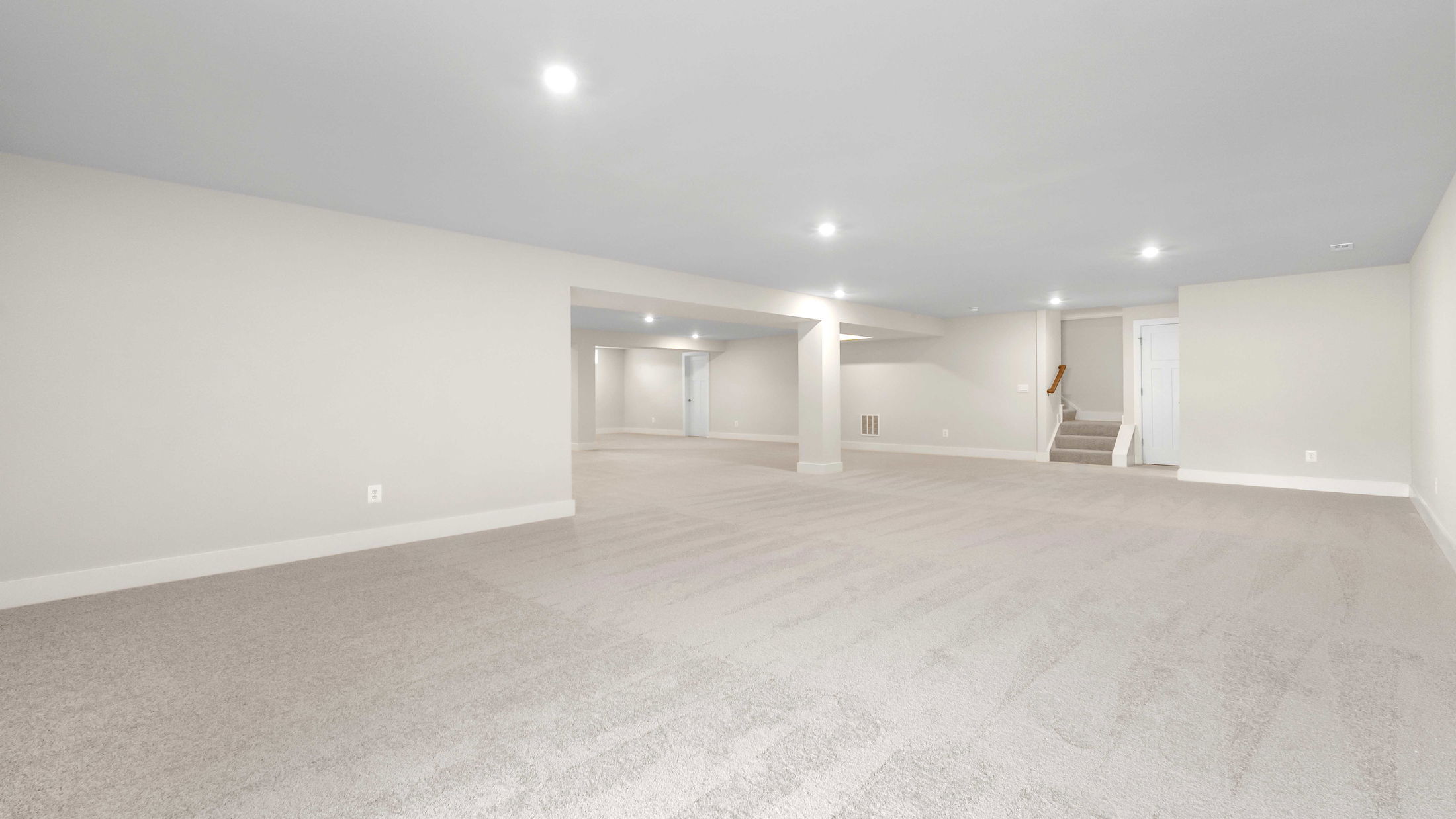 Spacious finished basement with plush carpeting, recessed lighting, and neutral walls leading to a staircase.