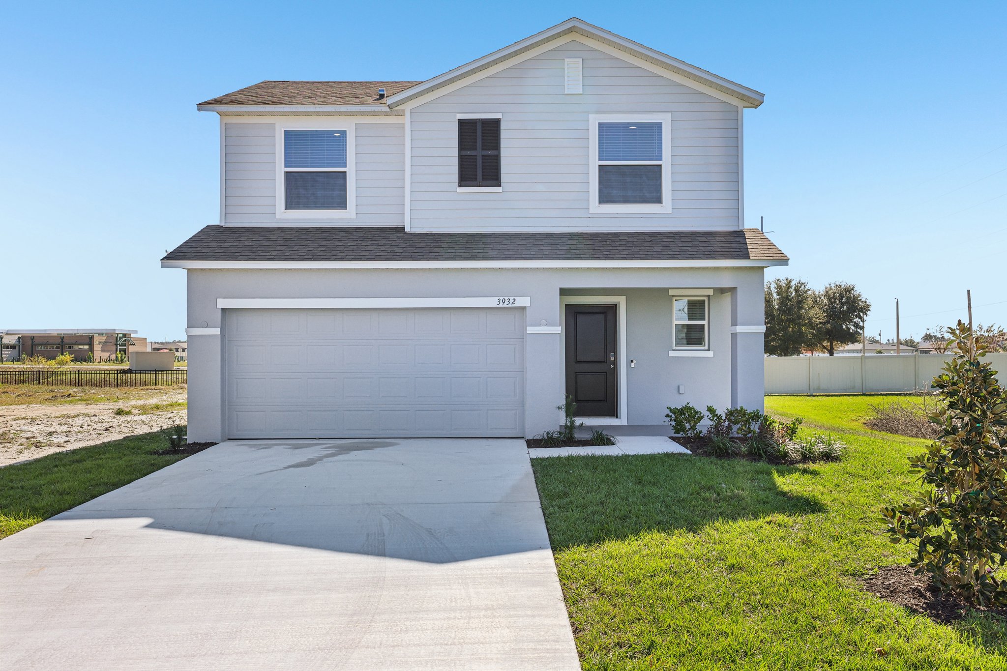Modern two-story house with a well-maintained lawn and spacious driveway against a clear blue sky.