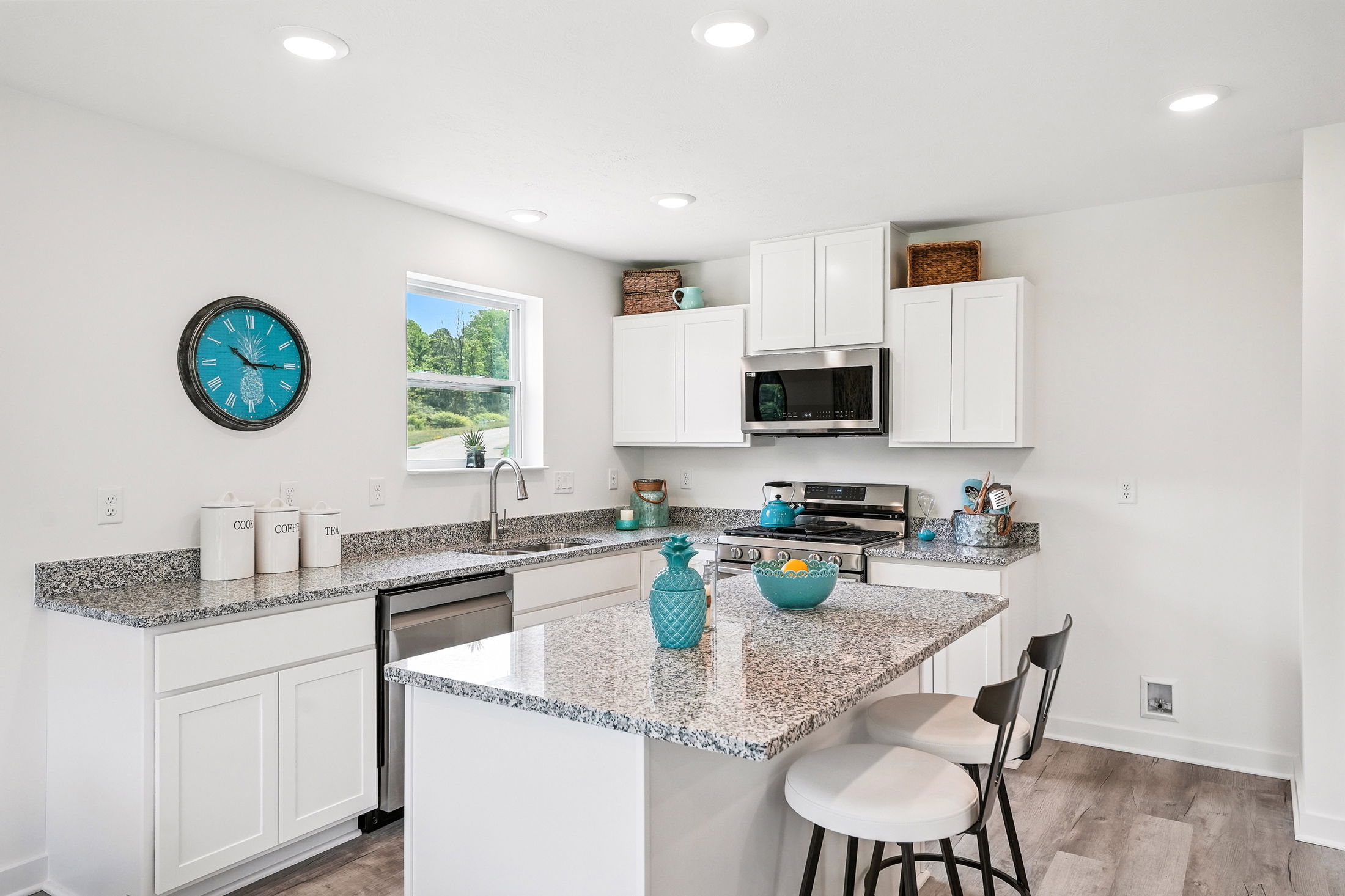 A modern kitchen with granite countertops, white cabinets, stainless steel appliances, and turquoise accents.