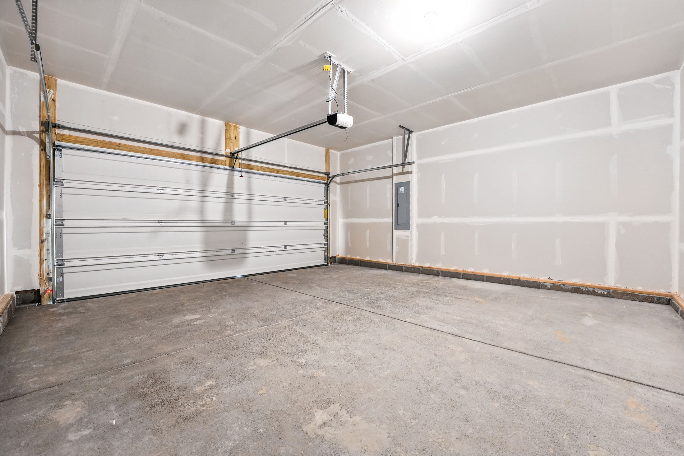 Empty, newly finished residential garage with white sectional garage door and concrete floor.