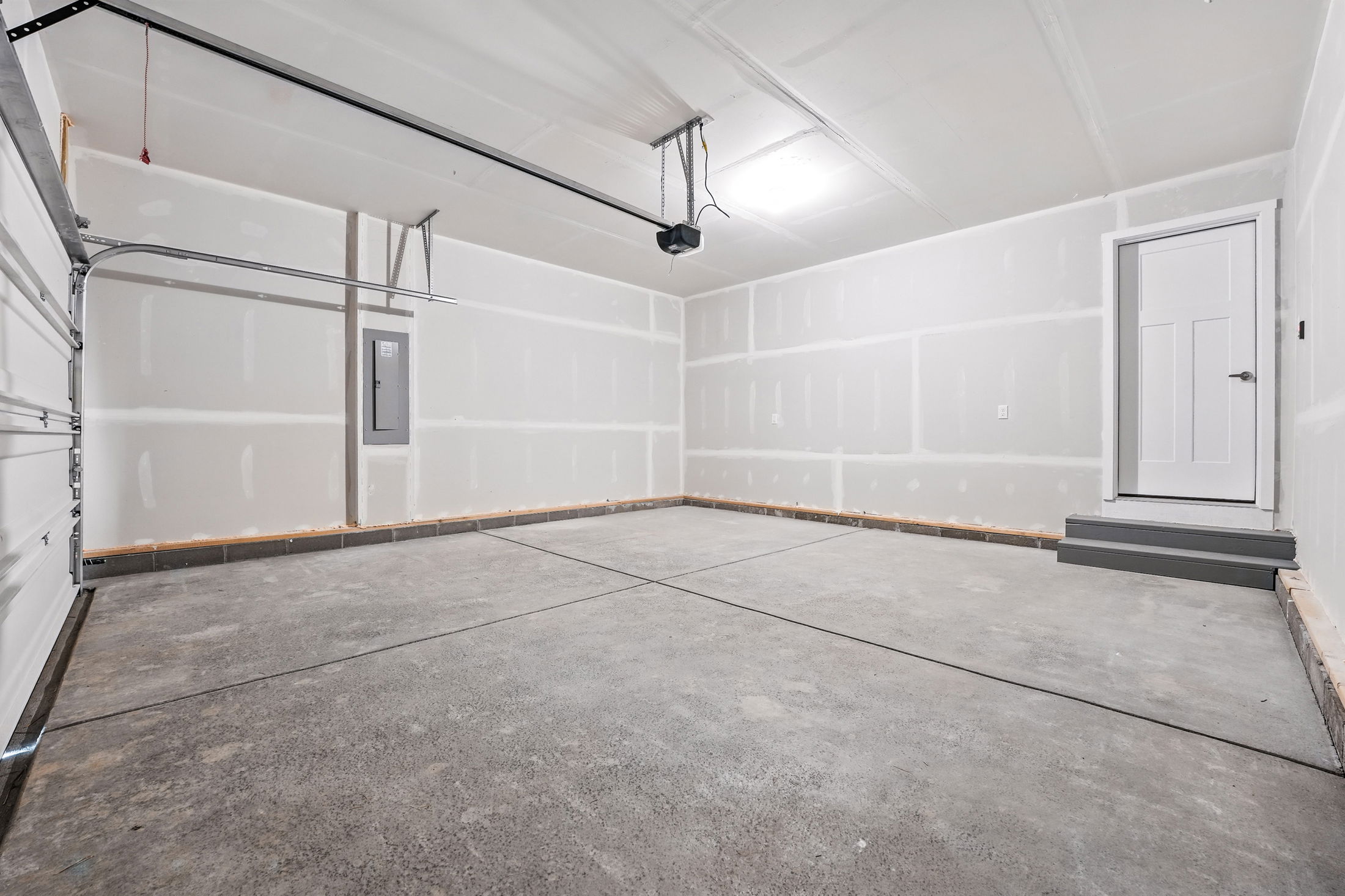 Empty, freshly painted garage interior with concrete floor, drywall, overhead door track, utility panel, and a white access door.