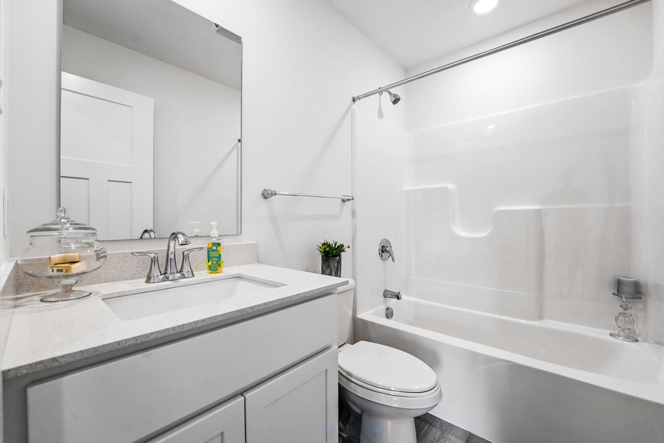 Modern white bathroom with a sleek vanity, large mirror, and a shower-tub combination.