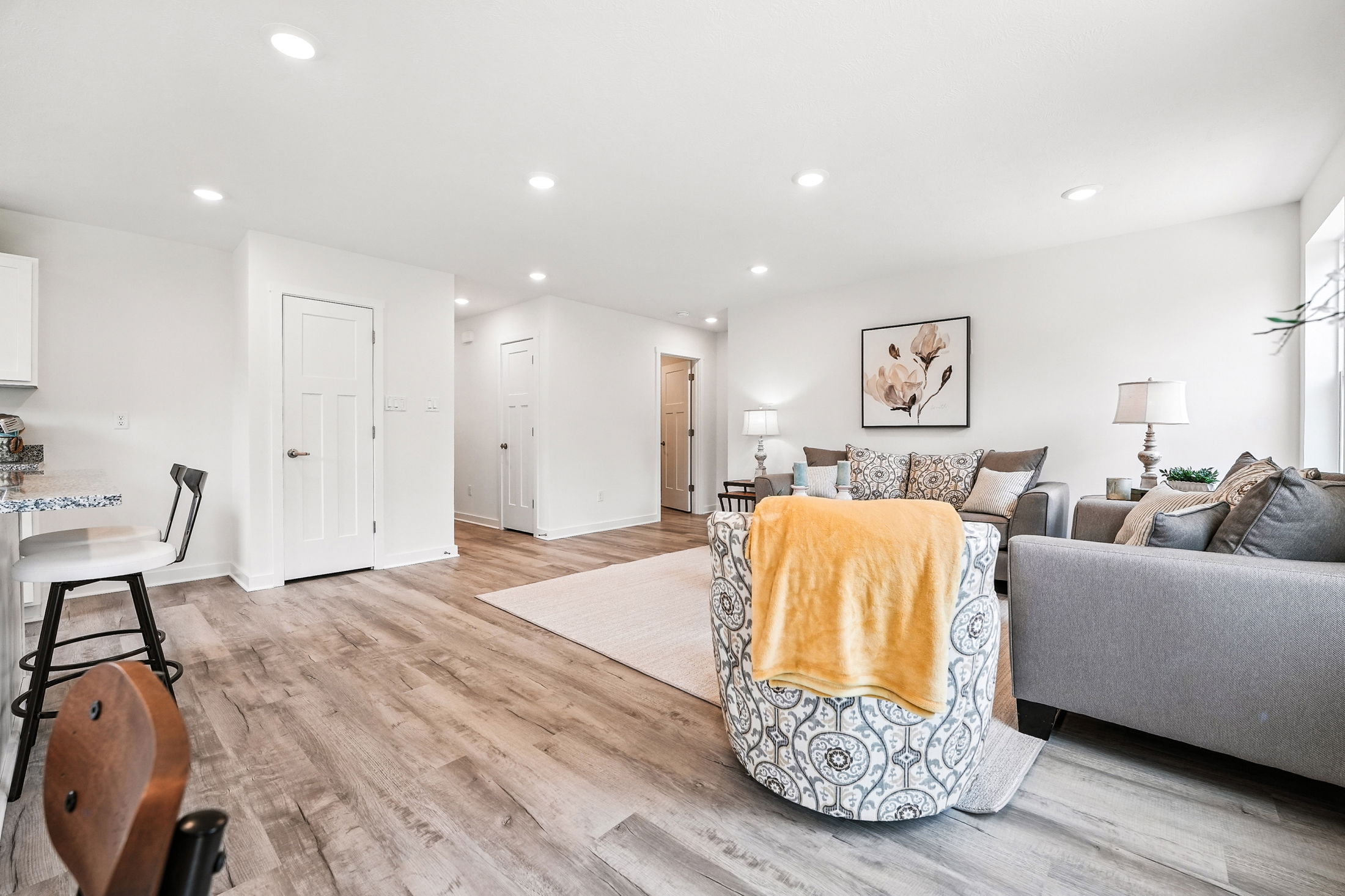 Stylish modern living room with gray sofas, floral-patterned chair, yellow throw blanket, hardwood floors, and soft lighting.