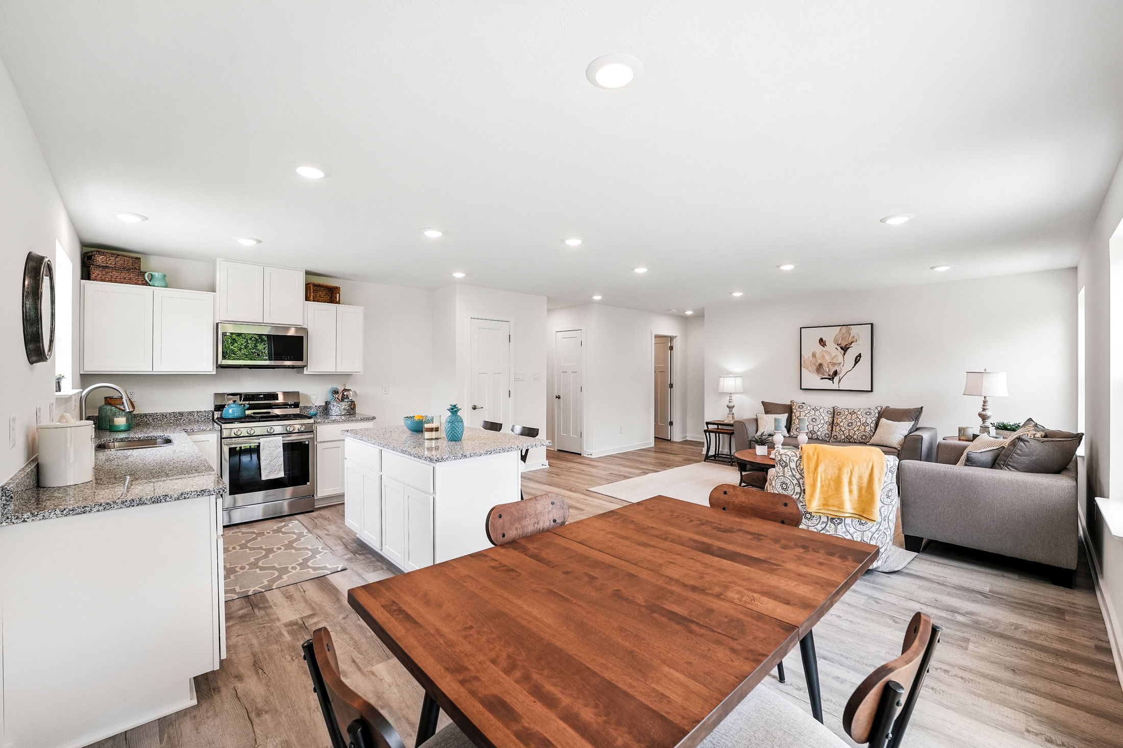 Open-concept modern living area with a kitchen, dining table, and cozy sitting space featuring neutral tones and wooden flooring.