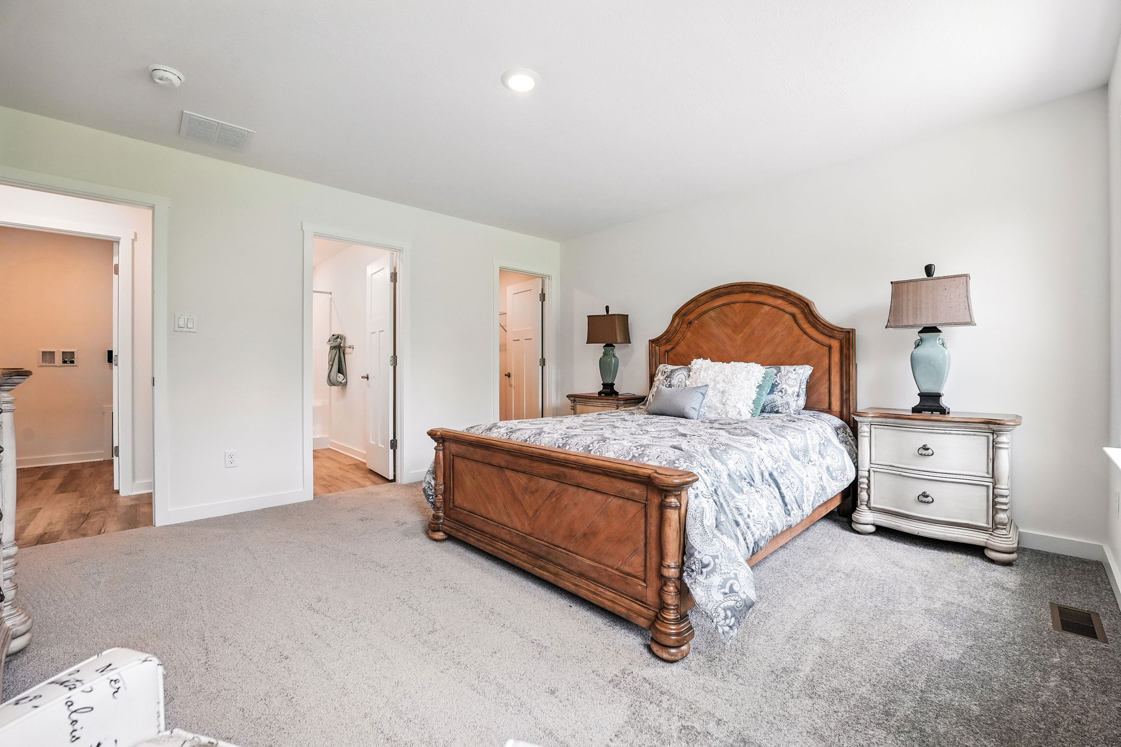 Elegant bedroom with a wooden bed frame, plush carpet, and stylish nightstands next to a bathroom entrance.