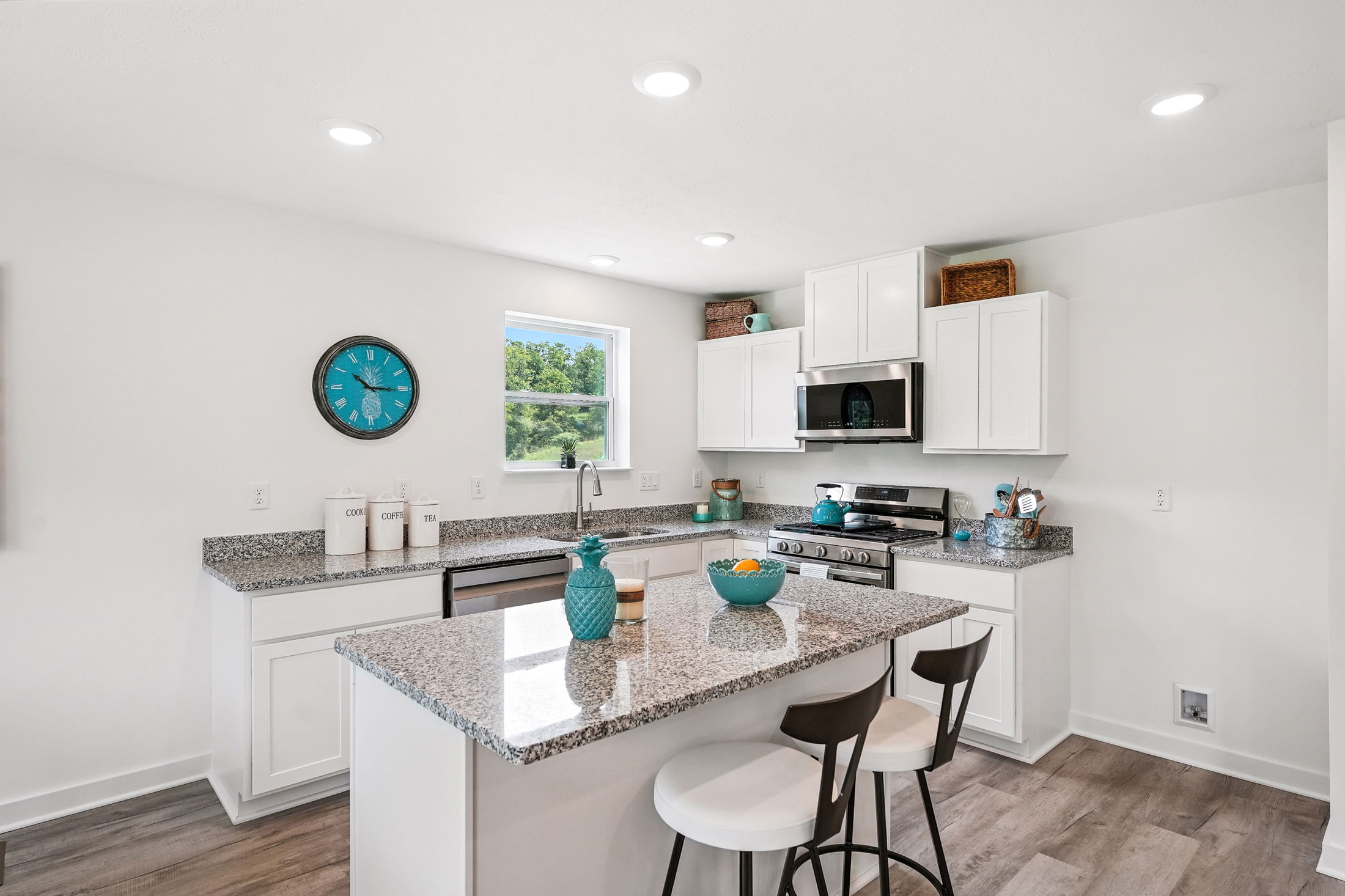 Modern kitchen with granite countertops, white cabinets, stainless steel appliances, and turquoise decor accents.