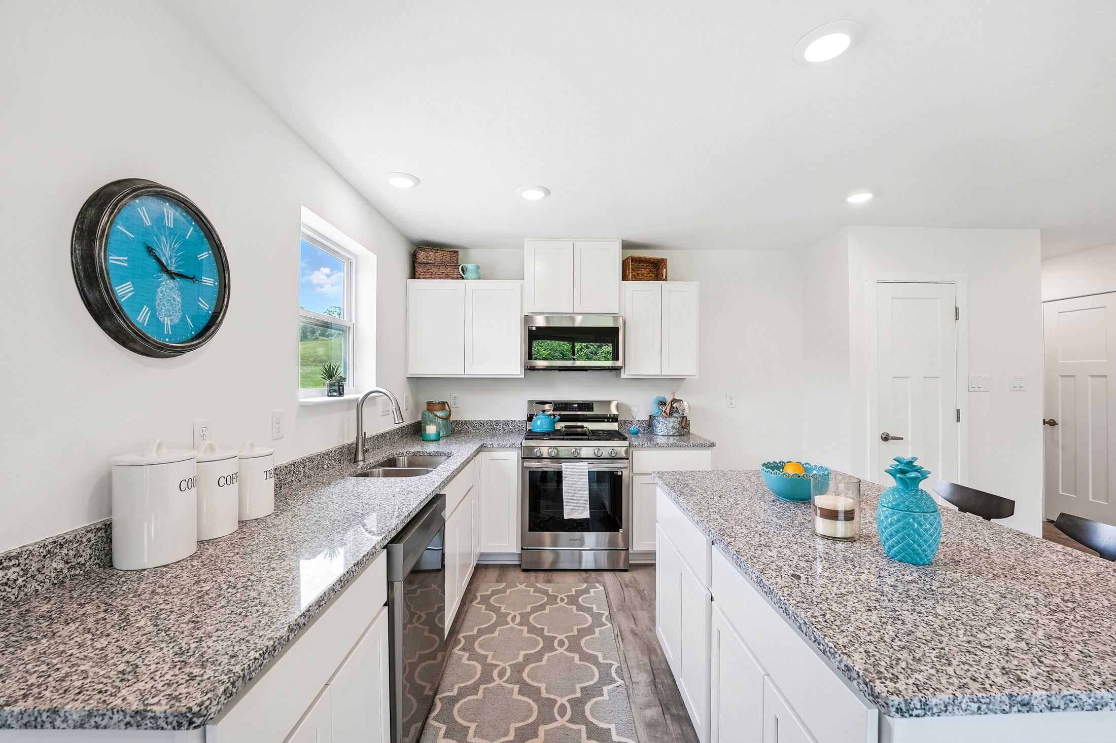 Modern kitchen with white cabinets, granite countertops, and teal accents, featuring stainless steel appliances and decorative wall clock.