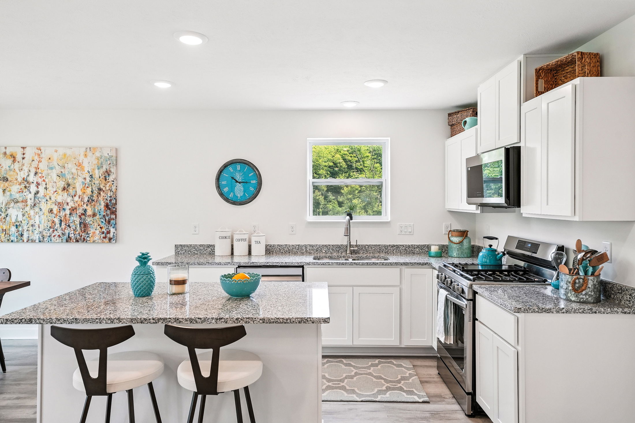 Modern kitchen with granite countertops, white cabinetry, and teal accents including a wall clock and decor.