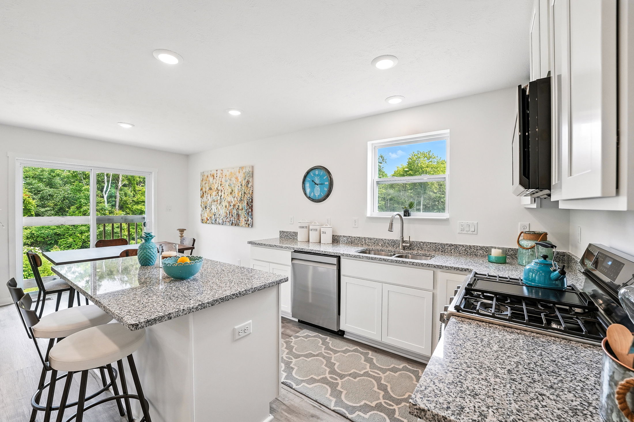 Modern kitchen interior with granite countertops, stainless steel appliances, and large windows overlooking green trees.