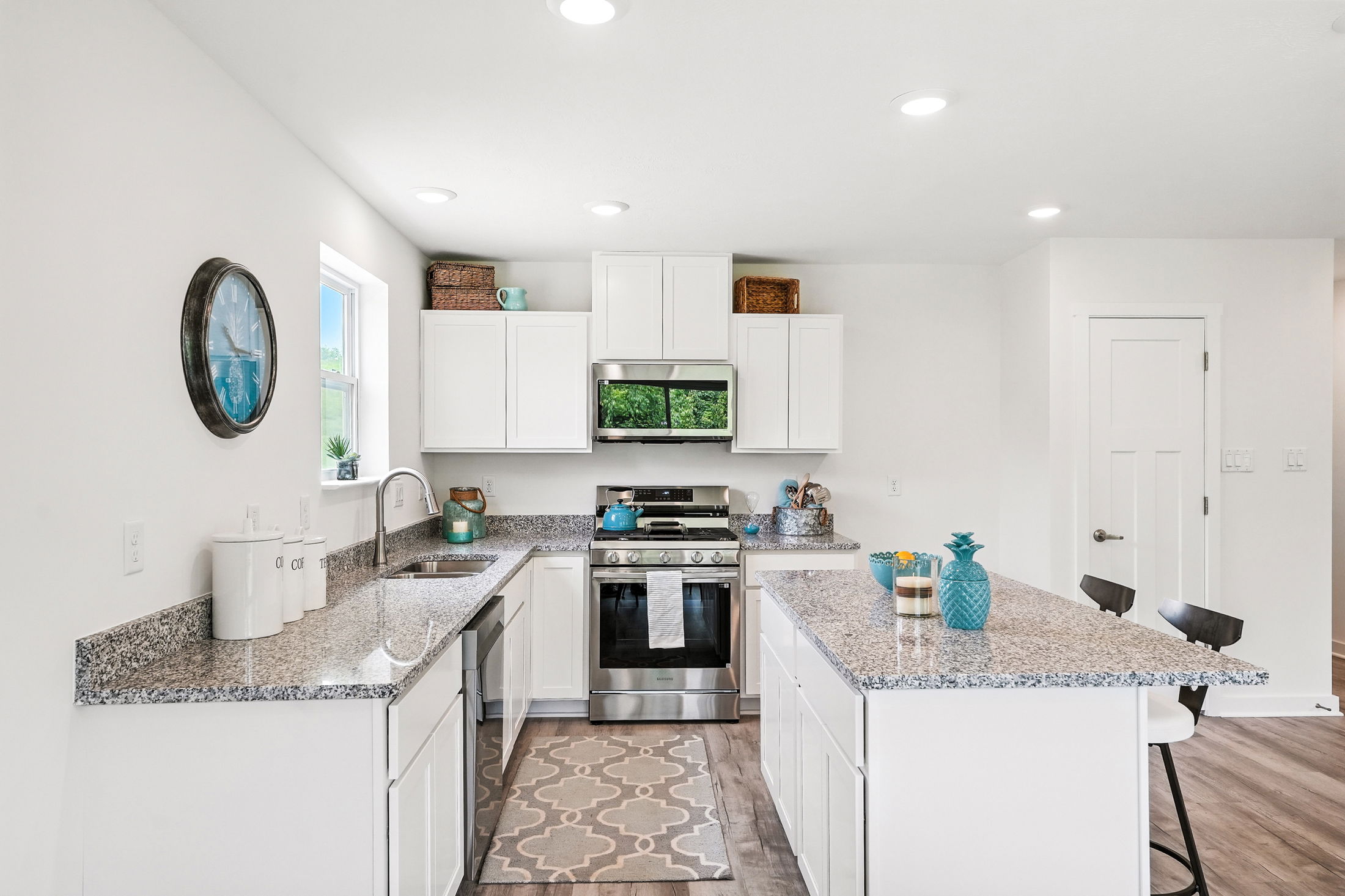 Modern white kitchen with granite countertops, stainless steel appliances, and decorative blue accents.