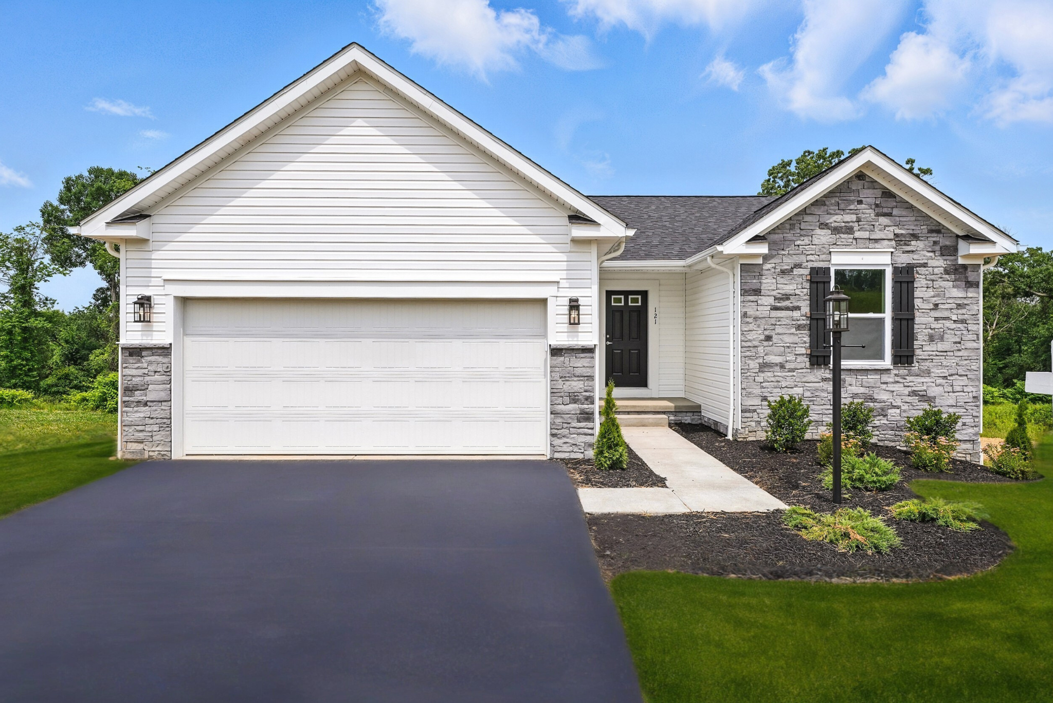 Modern suburban house with white siding and stone accents, featuring a two-car garage and neatly landscaped front yard under a blue sky.