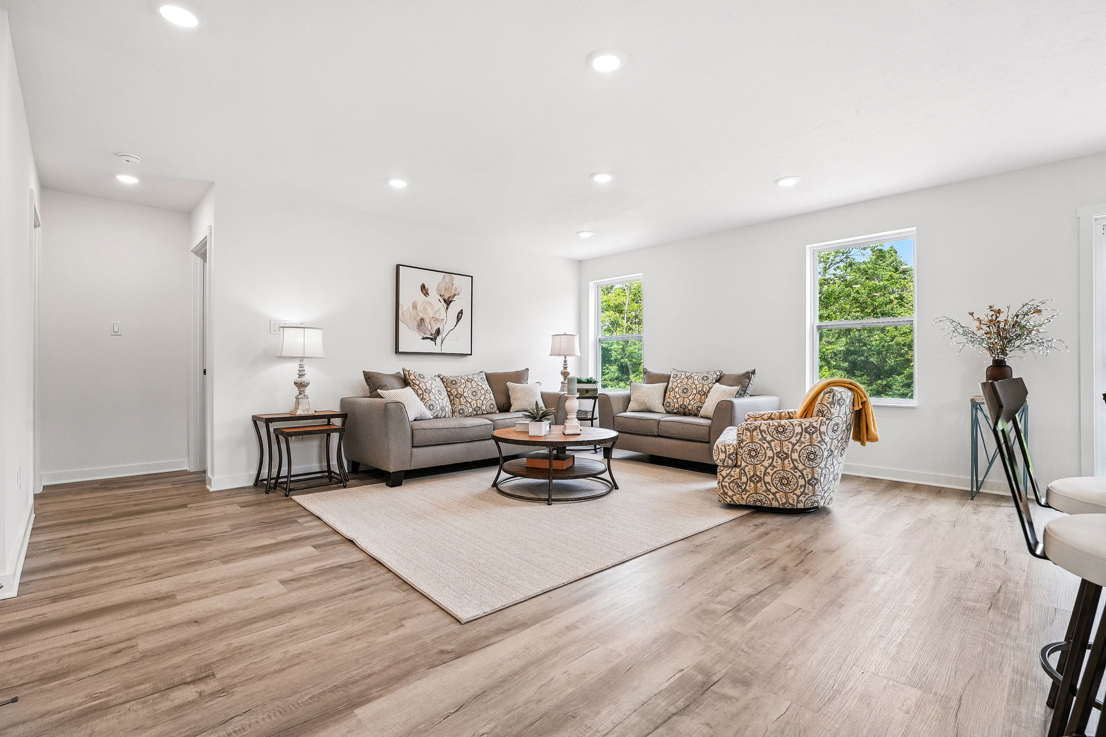 Modern living room with gray sofas, patterned armchair, light wood flooring, and large windows providing natural light.