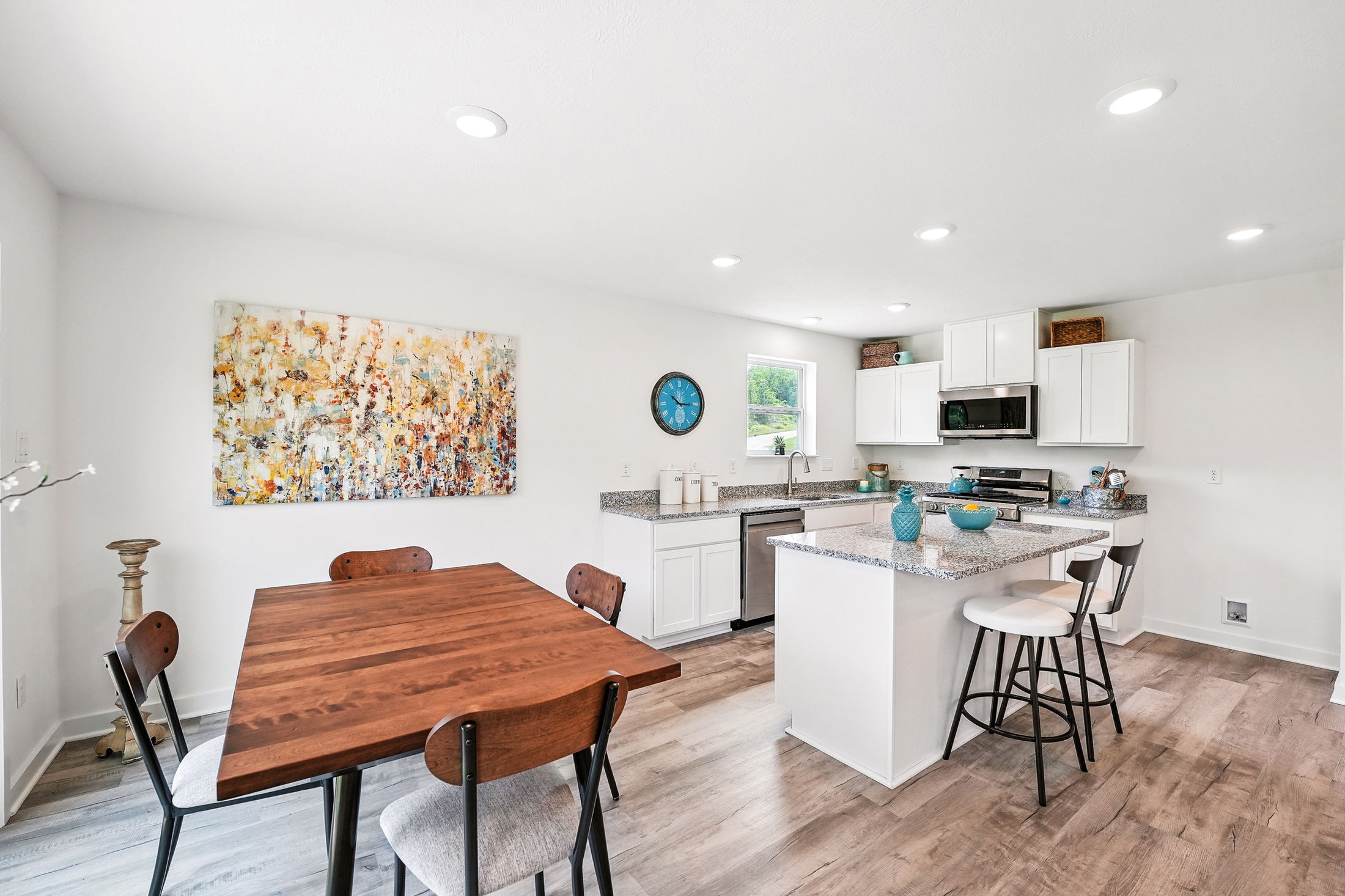 Bright modern kitchen and dining area with wooden table, abstract art, and white cabinetry.