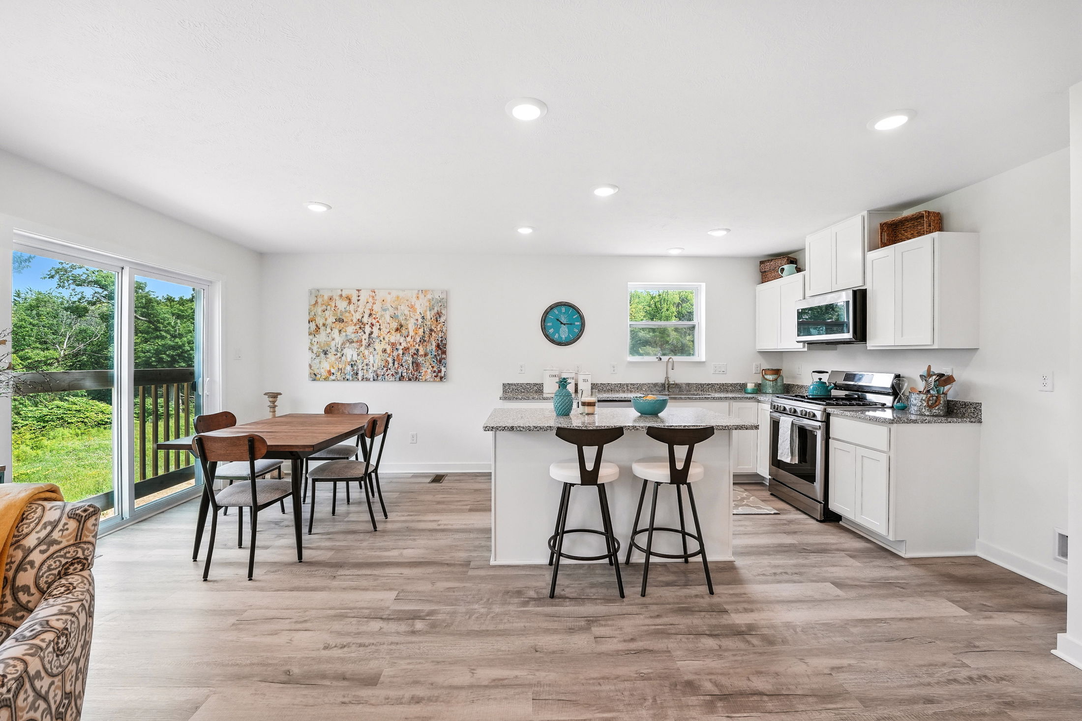Modern kitchen and dining area with white cabinets, granite countertops, and a view of greenery through sliding glass doors.