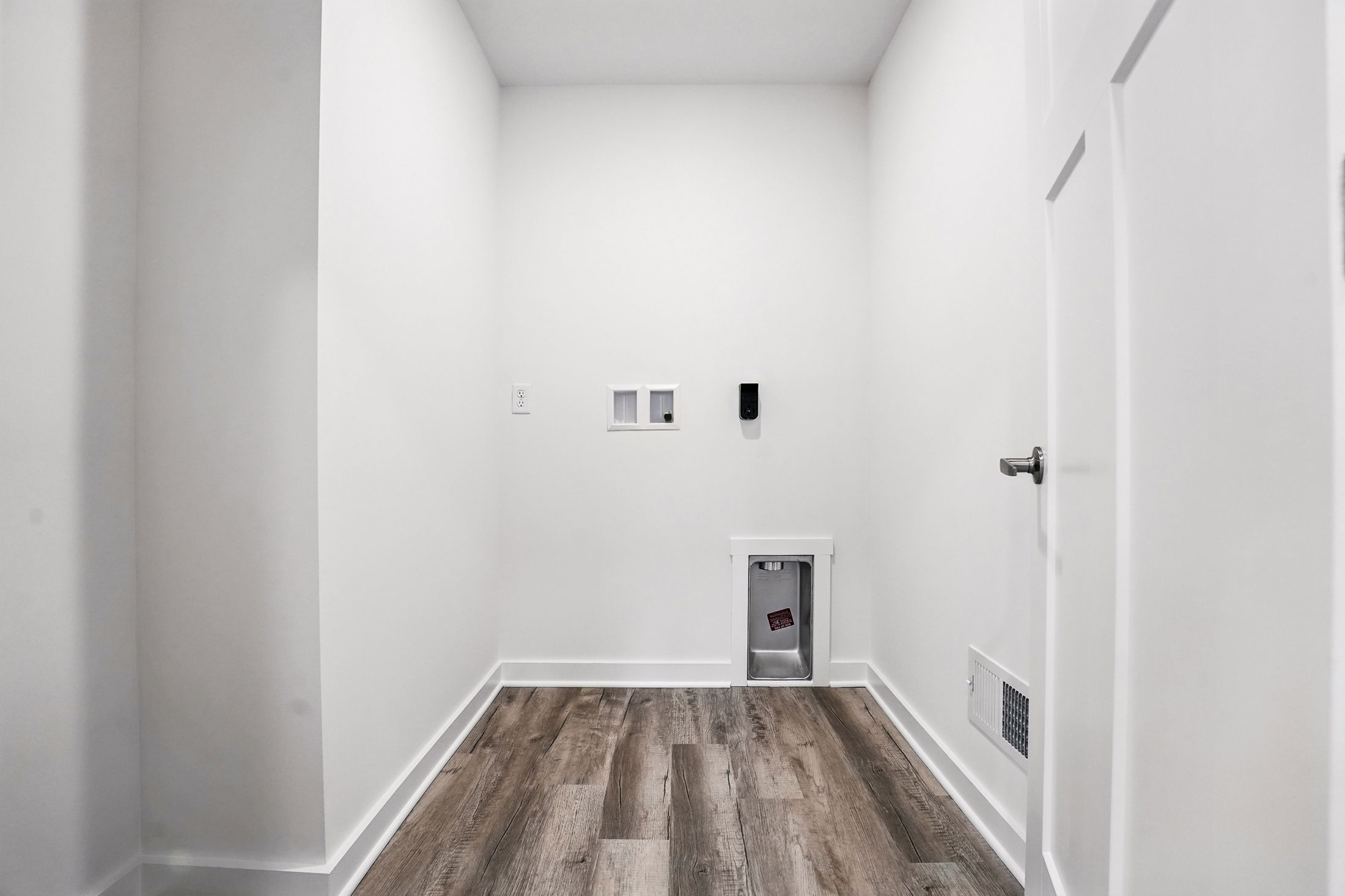 Modern laundry room with white walls and hardwood floors featuring washer and dryer hookups.