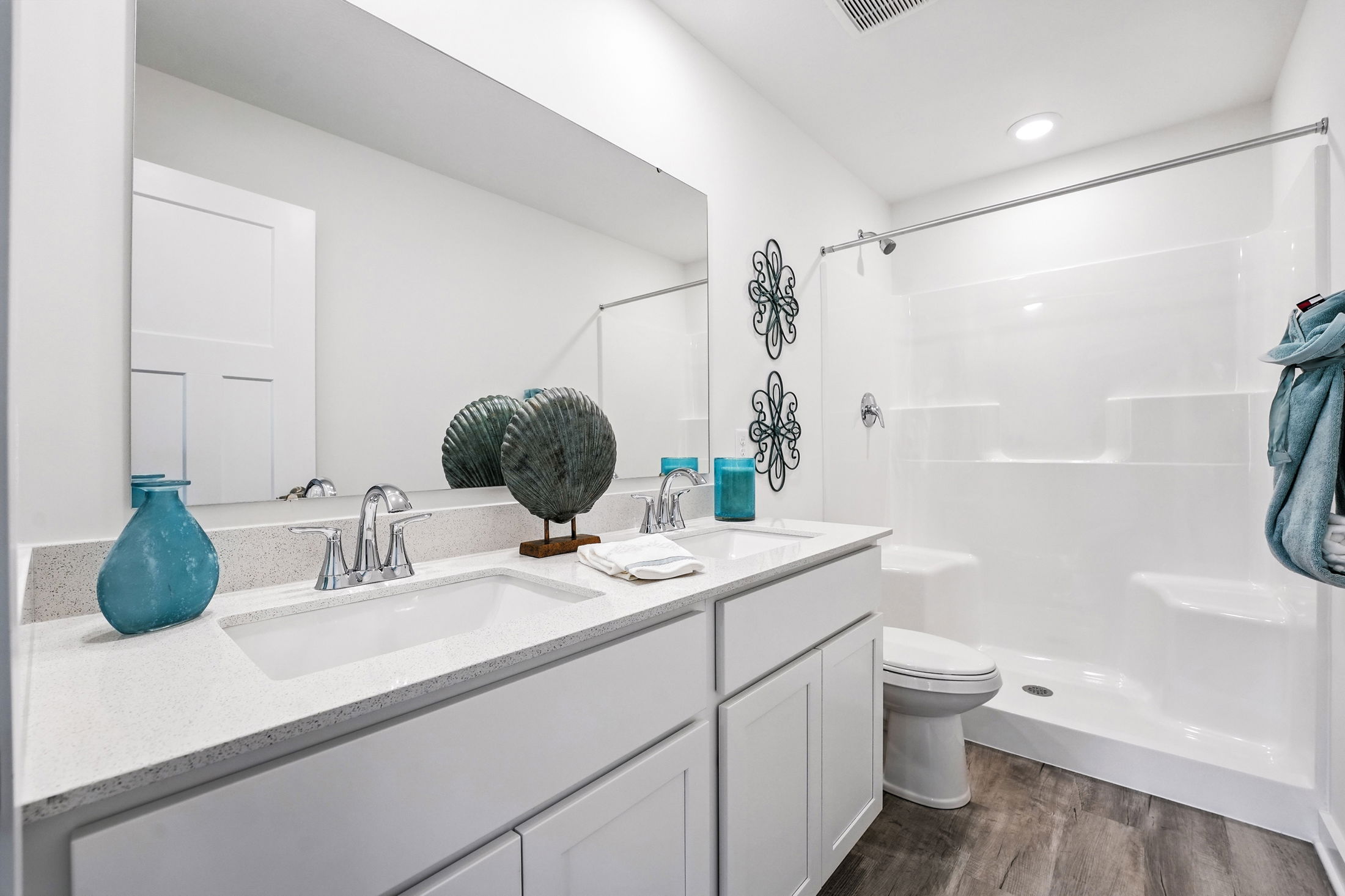 Modern white bathroom with dual sinks, decorative metal wall art, and blue accents.