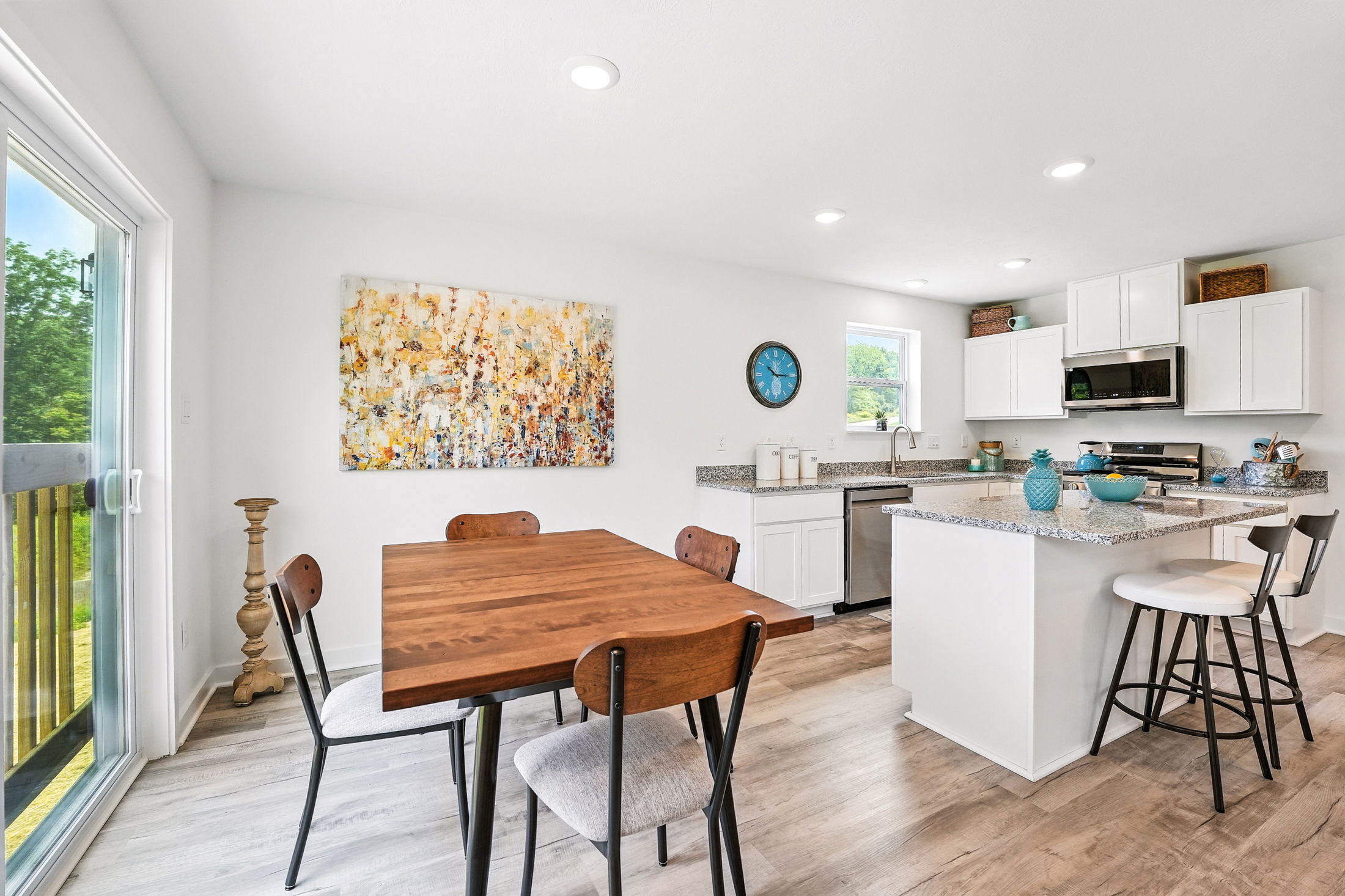 Modern kitchen and dining area with white cabinets, granite countertops, wooden dining table, and large abstract artwork on the wall.