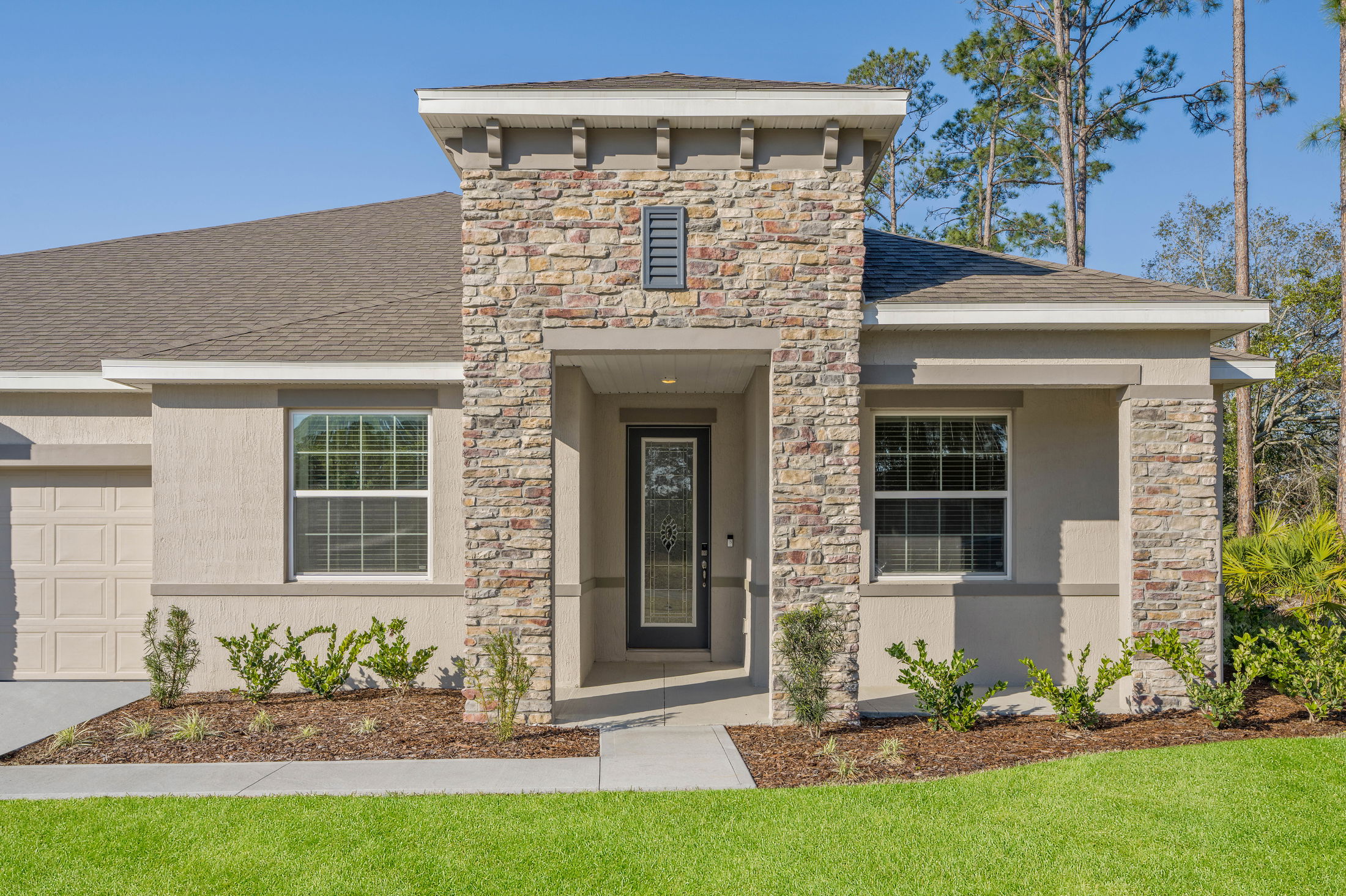 Front view of a modern home with stone facade, manicured lawn, and pathway leading to the entrance.