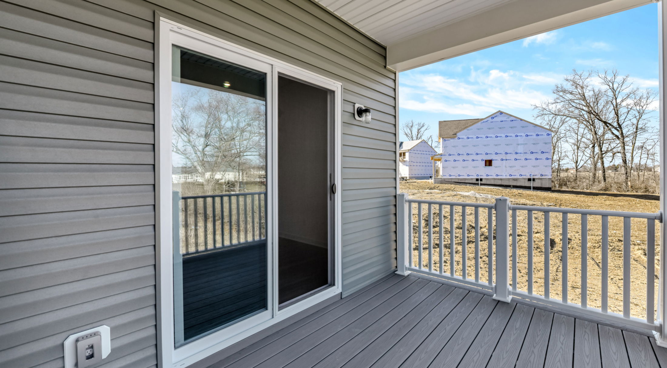 Modern gray vinyl-sided porch with sliding glass door and white railing overlooking construction.