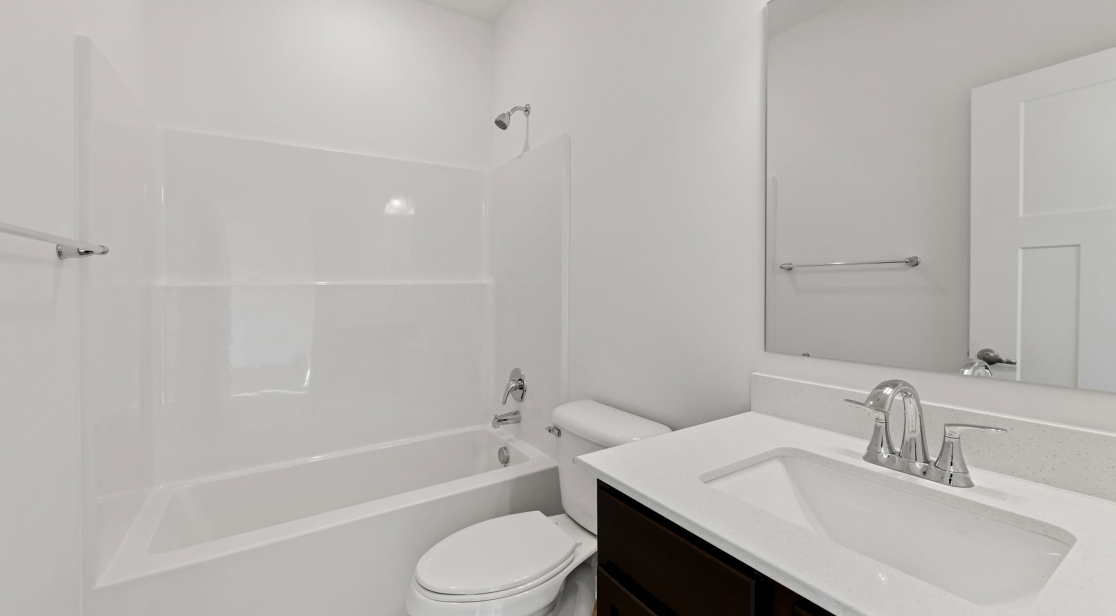 Modern bathroom with white bathtub, sink, and toilet featuring chrome fixtures.