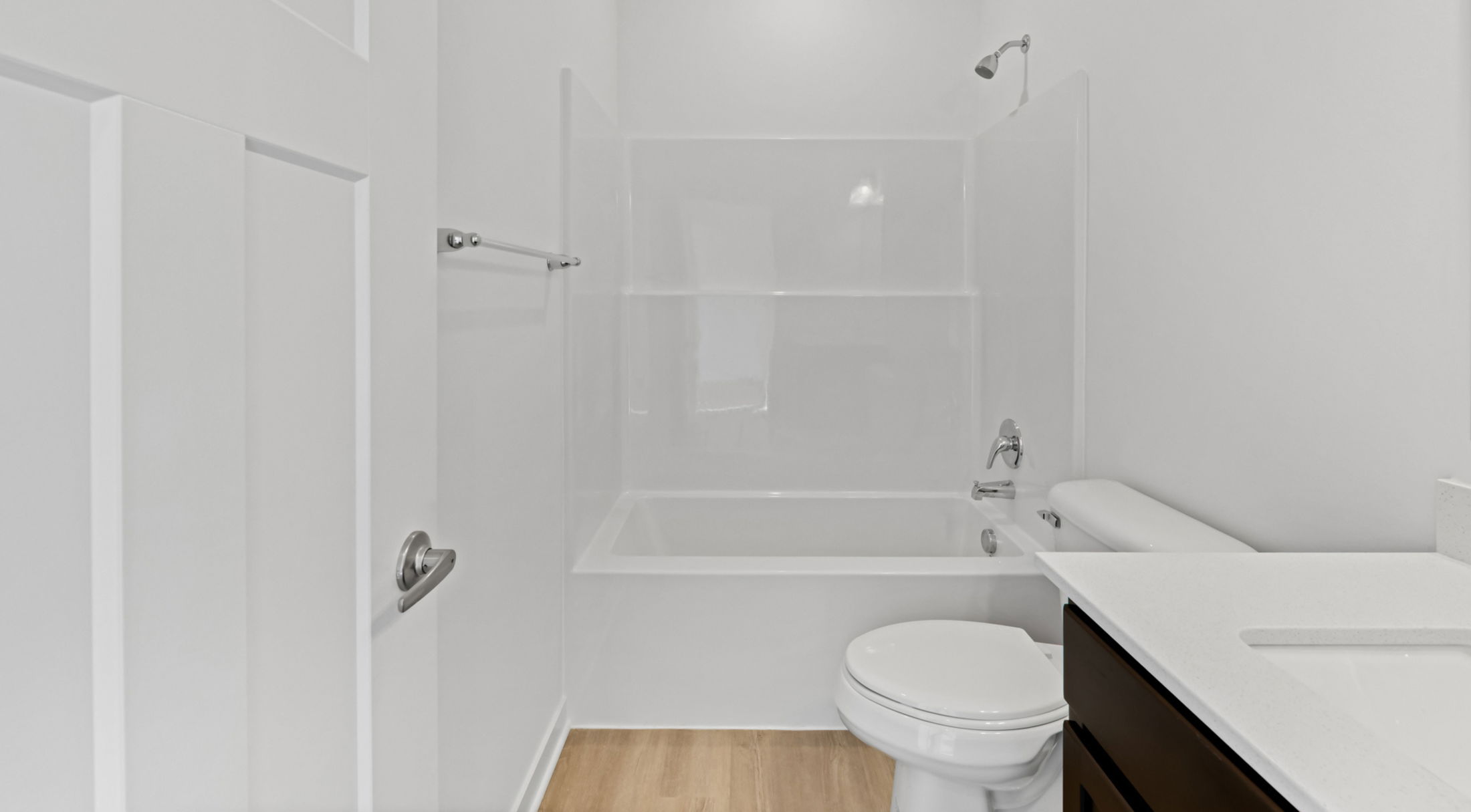 Minimalist white bathroom with a modern bathtub, toilet, sink, and wooden flooring.