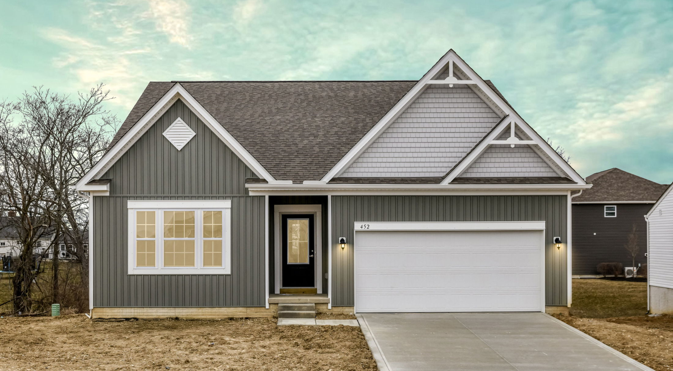 Newly constructed grey house with a gable roof, large windows, and a two-car garage under a blue sky.