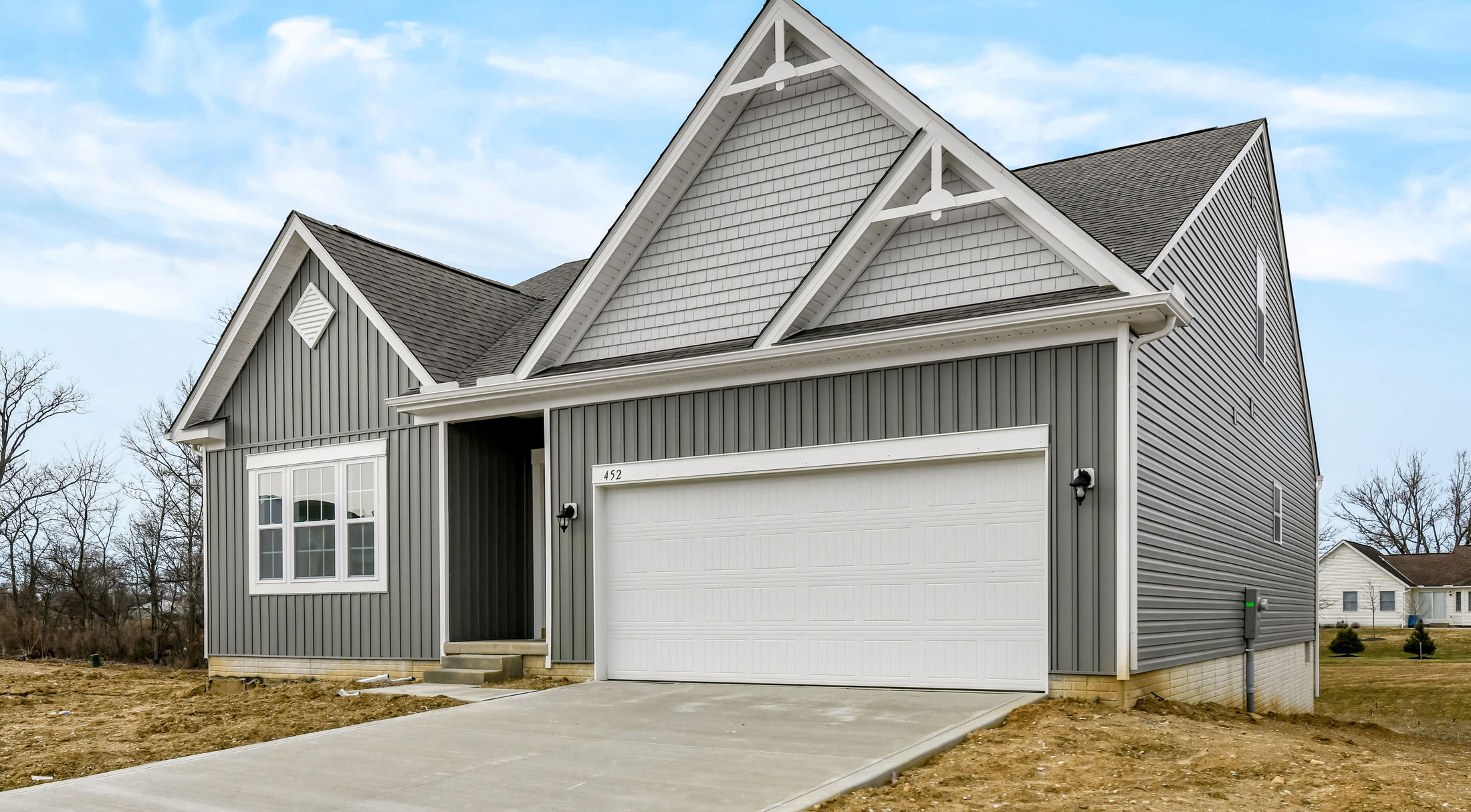 Modern gray single-story house with white garage and pitched roof against a clear blue sky.