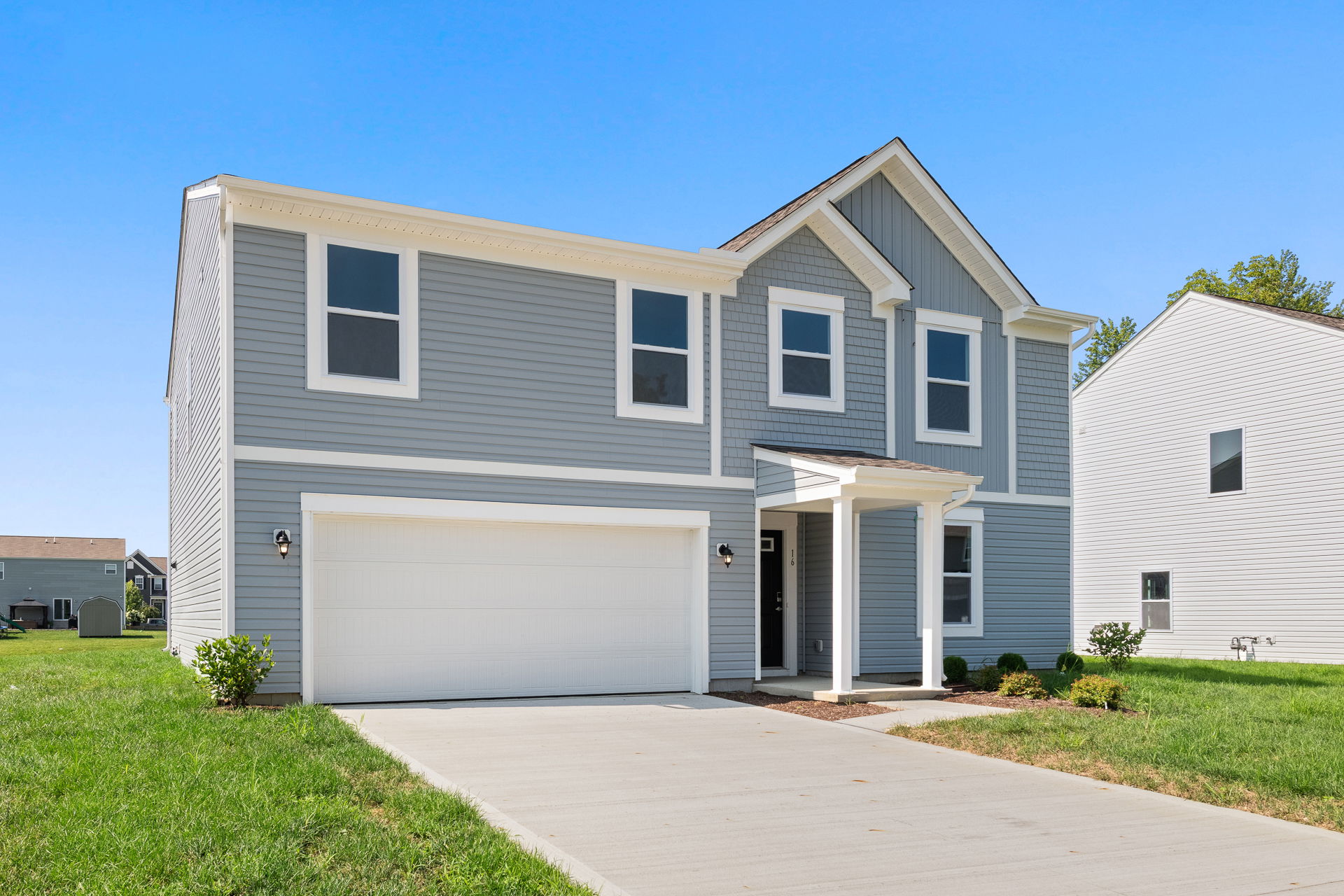 Two-story modern grey house with a white garage and porch set against a clear blue sky.