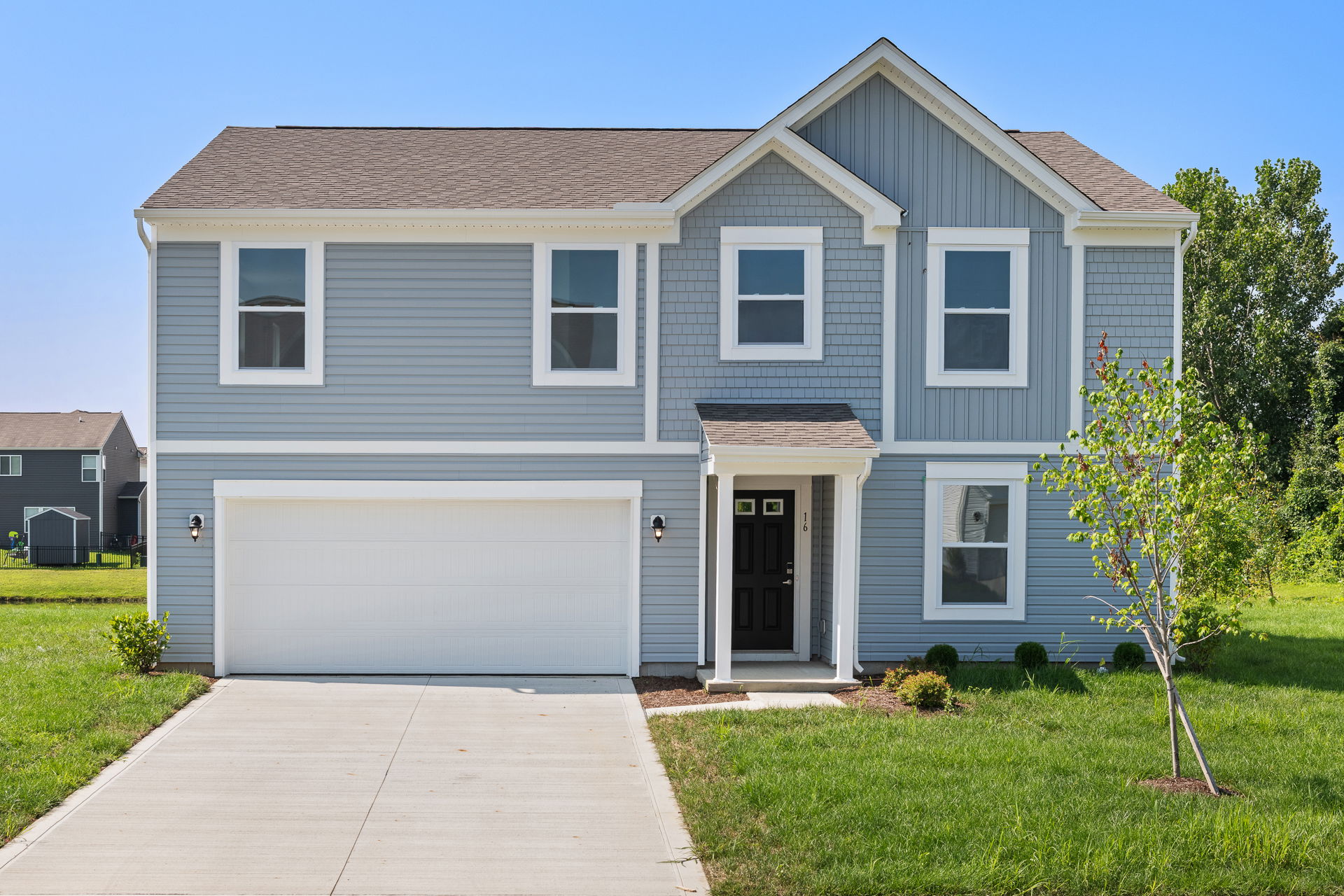 Modern two-story gray suburban home with a spacious driveway and a well-maintained lawn on a clear day.