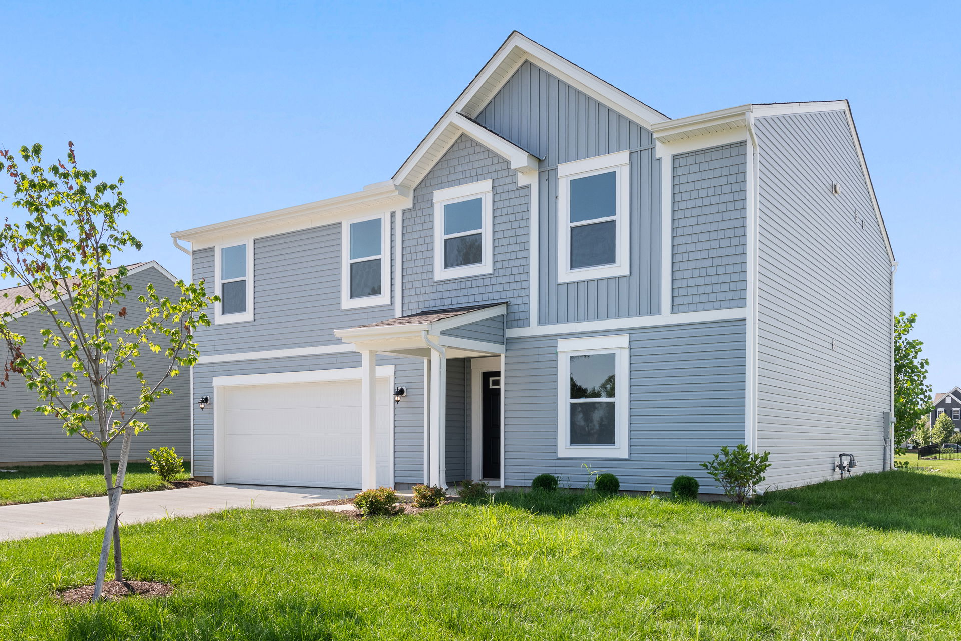 Modern two-story gray house with manicured lawn and driveway on a sunny day.