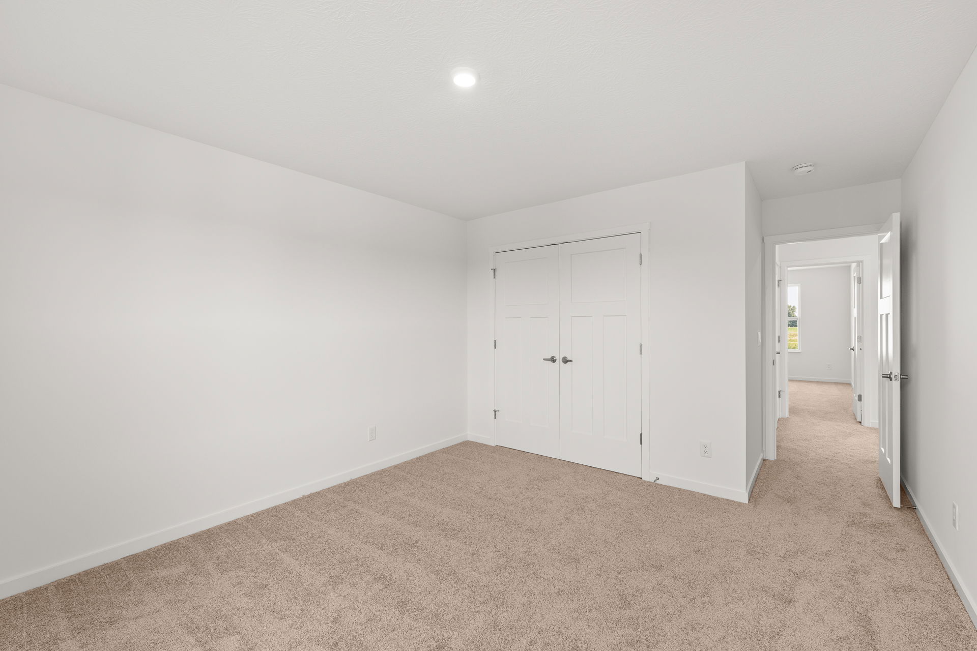 Empty modern bedroom with beige carpet, white walls, and a closed double door closet.