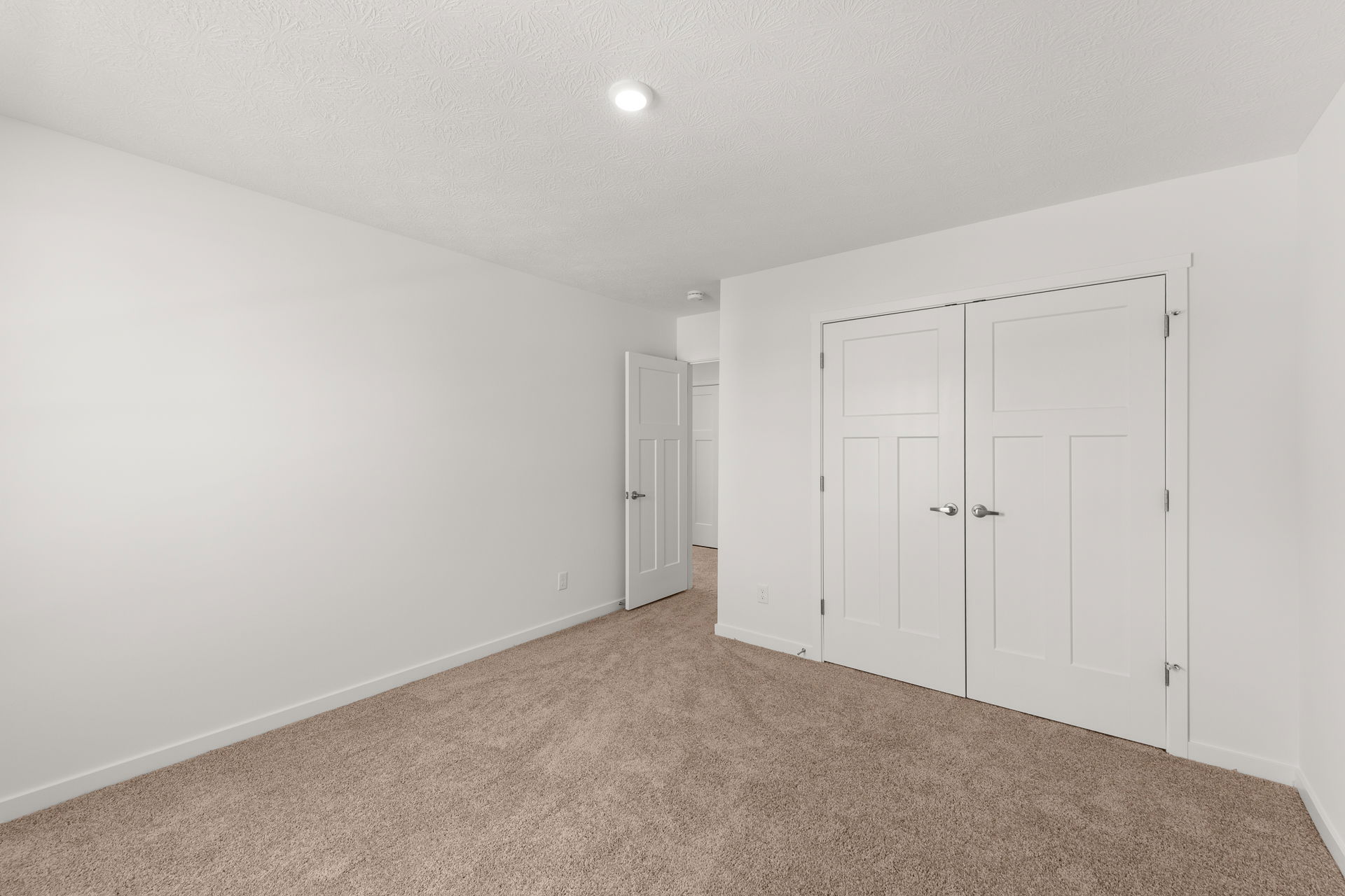 Empty room with beige carpet, white walls, a double-door closet, and an open white door.