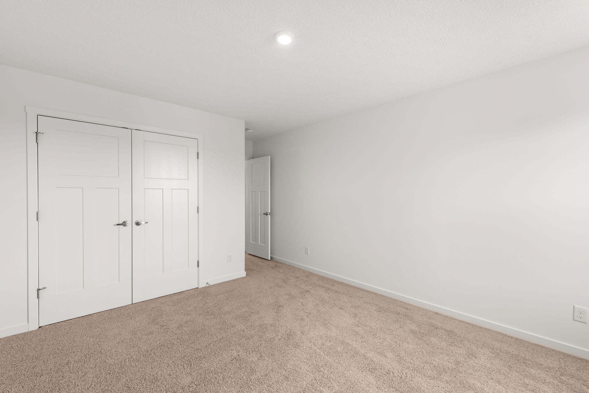 Modern empty room with beige carpet, white double closet doors, and soft overhead lighting.