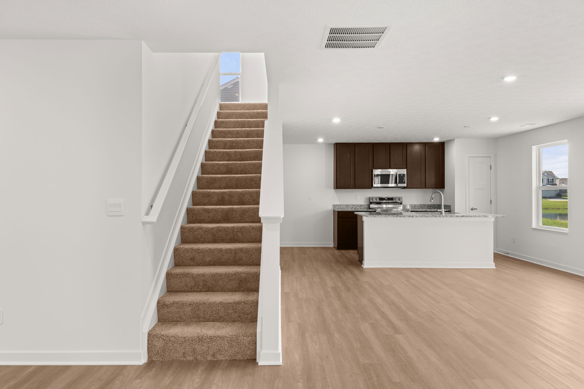 Modern open-concept kitchen and staircase in a new, unfurnished home interior.