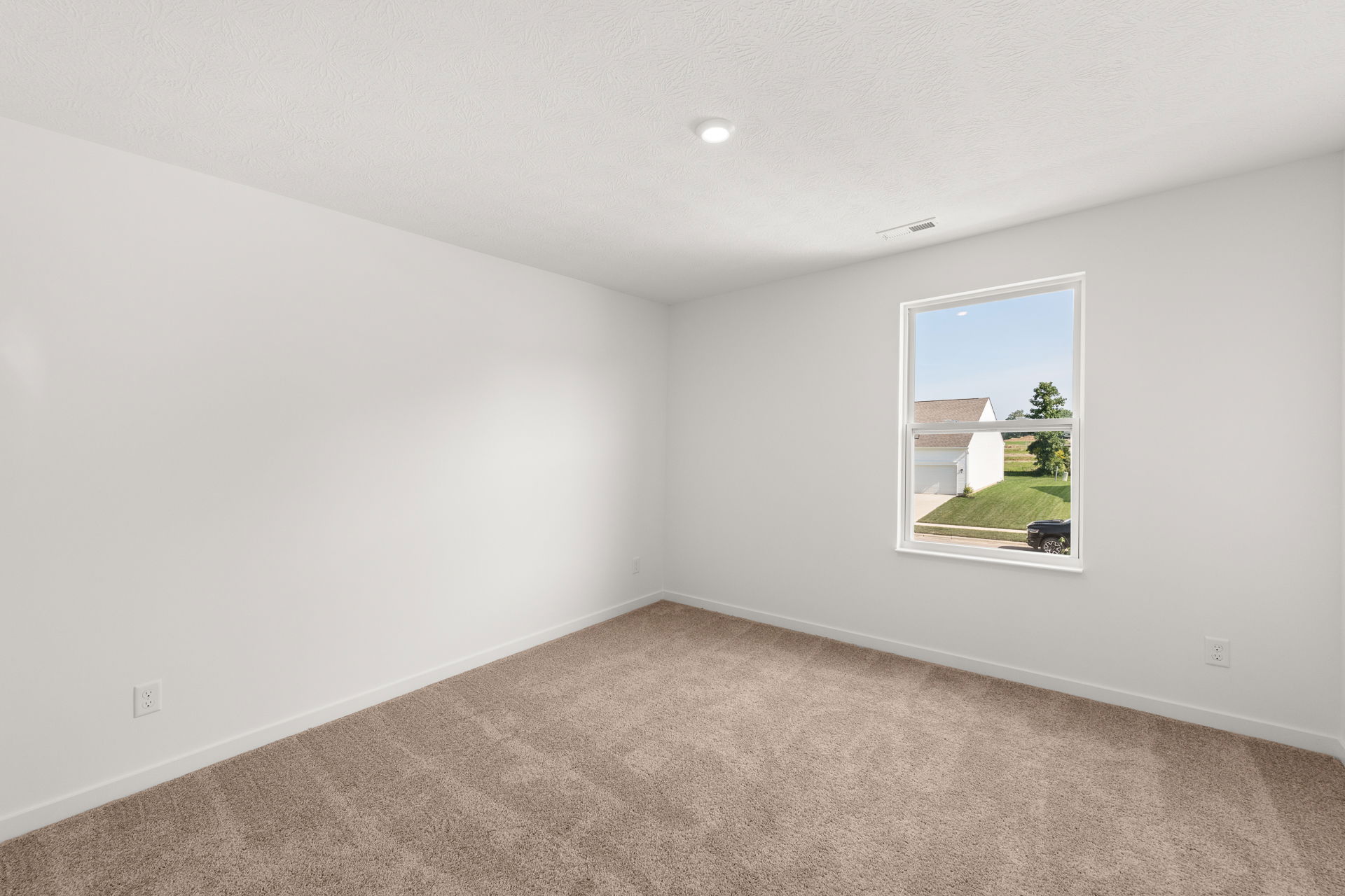 Empty room with beige carpet and white walls featuring a large window overlooking a suburban neighborhood.
