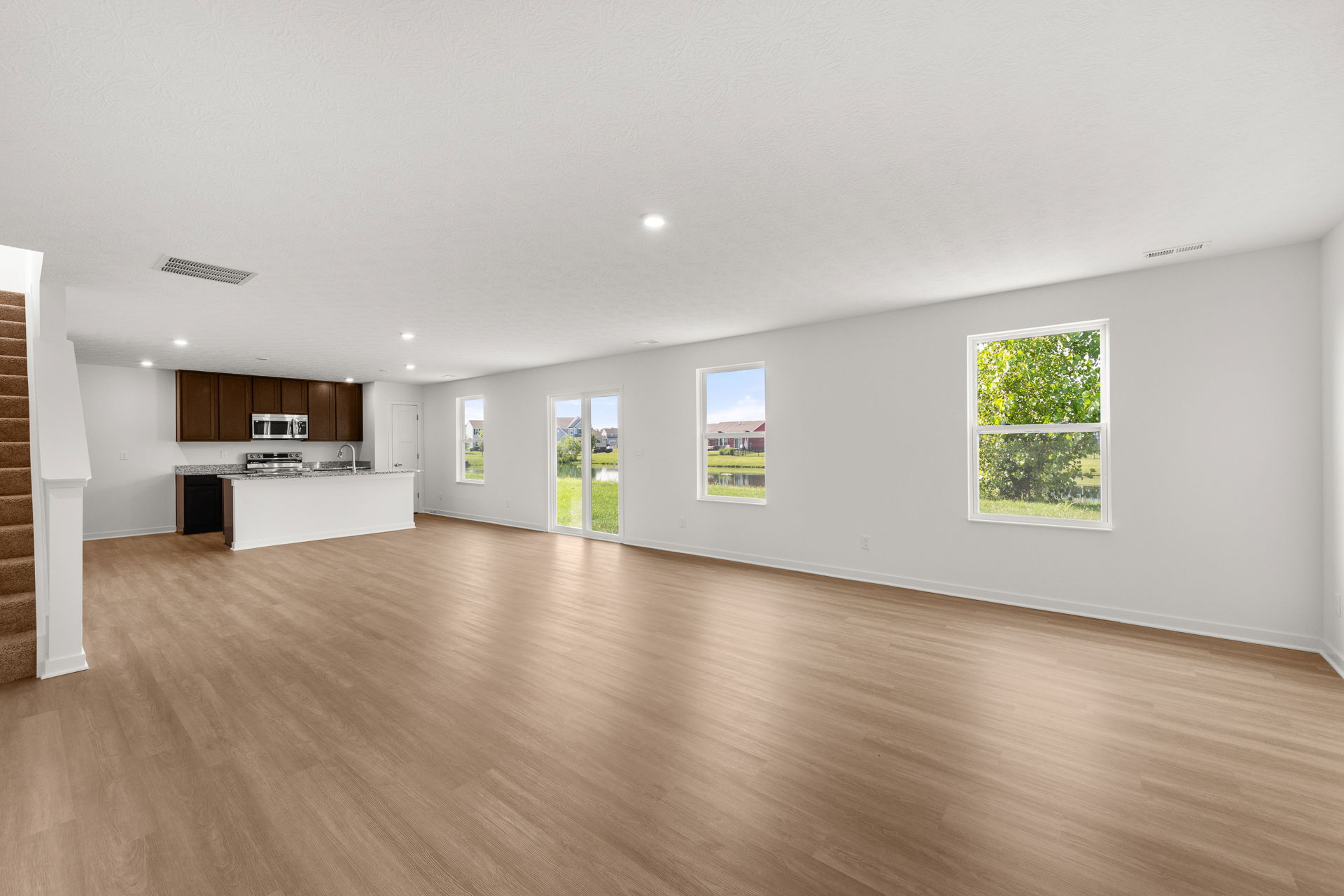 Spacious open-plan living room with modern kitchen, hardwood floors, and large windows with garden view.