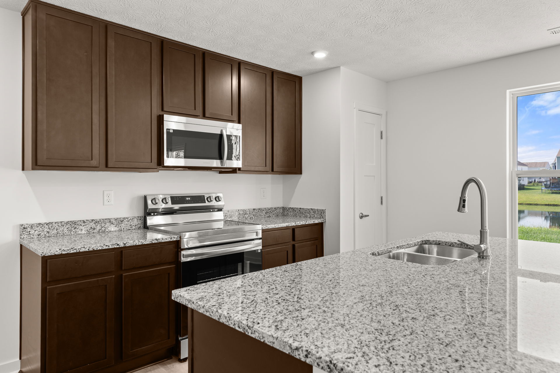 Modern kitchen with stainless steel appliances, granite countertops, and dark wooden cabinets, featuring a view of a scenic landscape through a window.