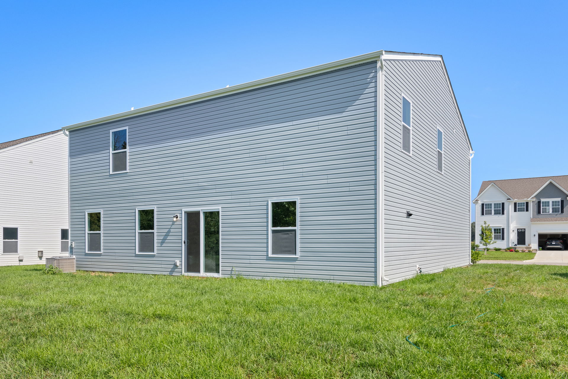 Modern two-story gray vinyl siding house with green lawn under a clear blue sky.