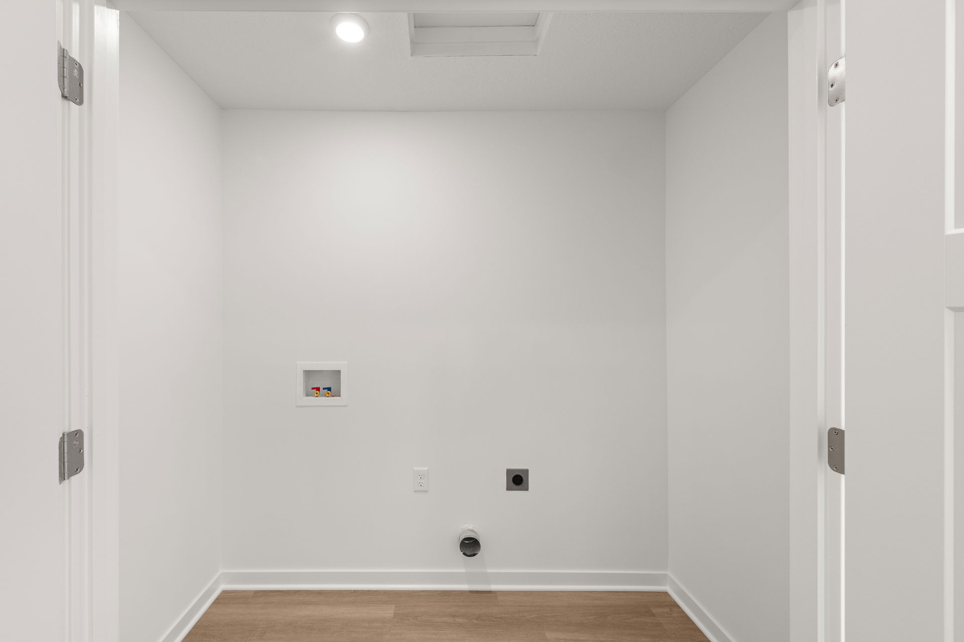 Empty laundry room with white walls, hardwood flooring, and a small recessed compartment.