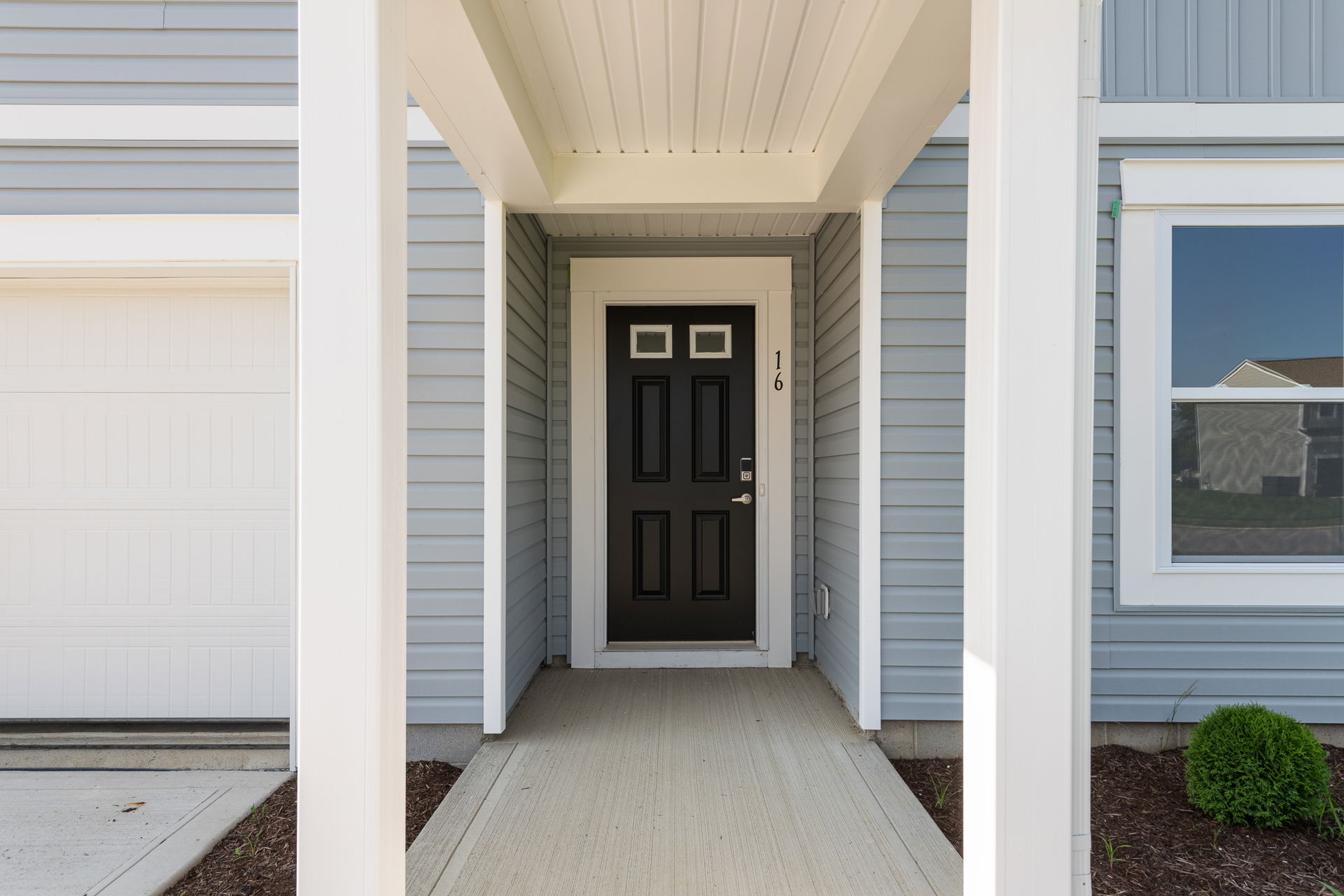 Entryway of a modern home featuring a black front door and light gray siding.