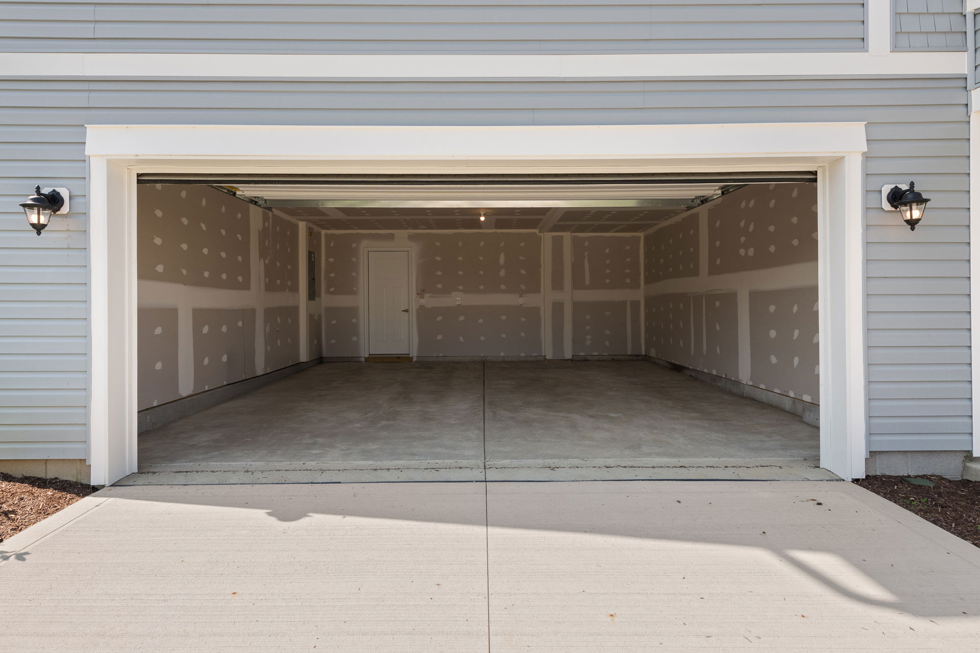 Empty garage interior with unfinished drywall, concrete flooring, and a side door, showcasing modern home storage potential.