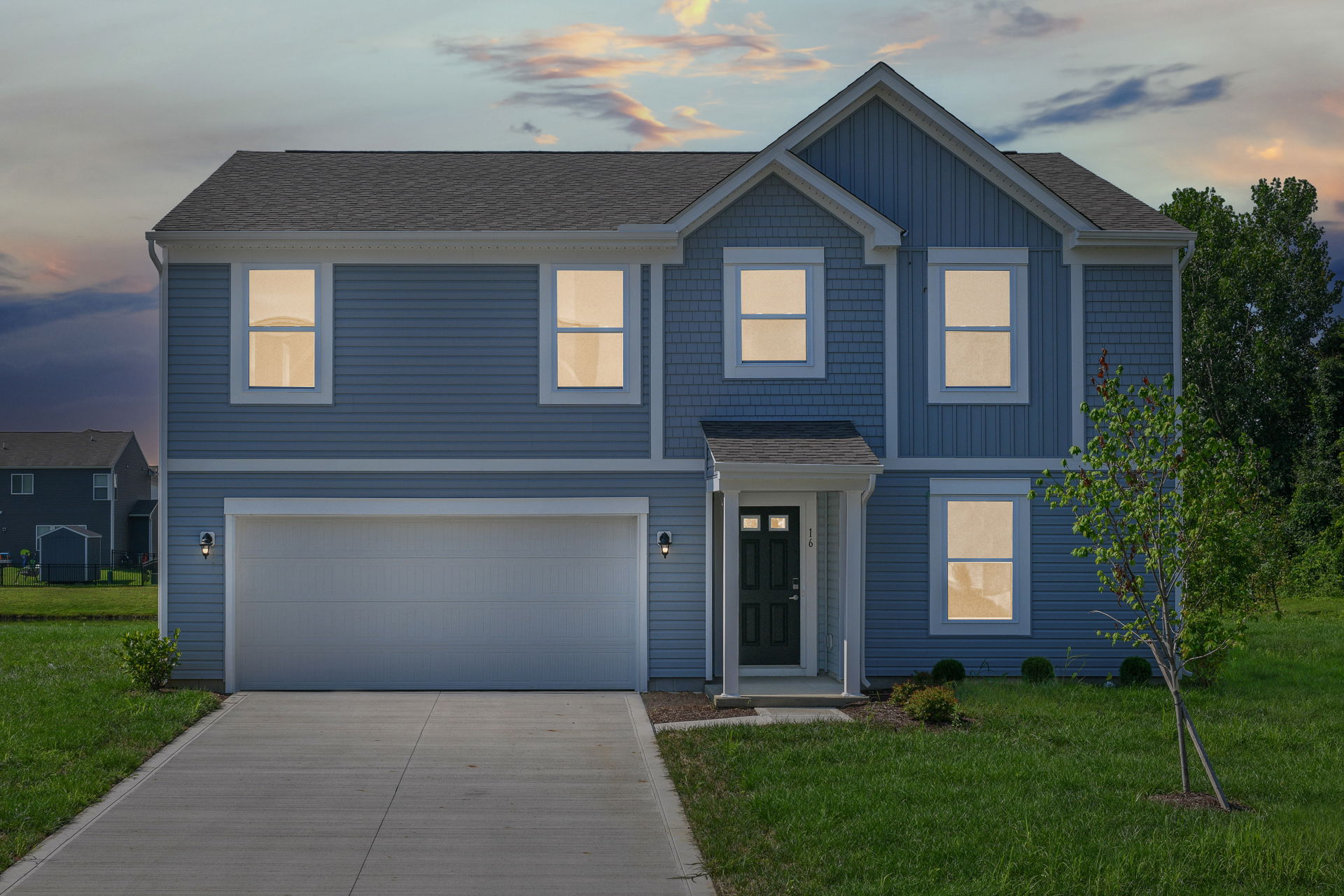 A modern two-story blue house with white trim and a welcoming front porch set against a sunset sky.