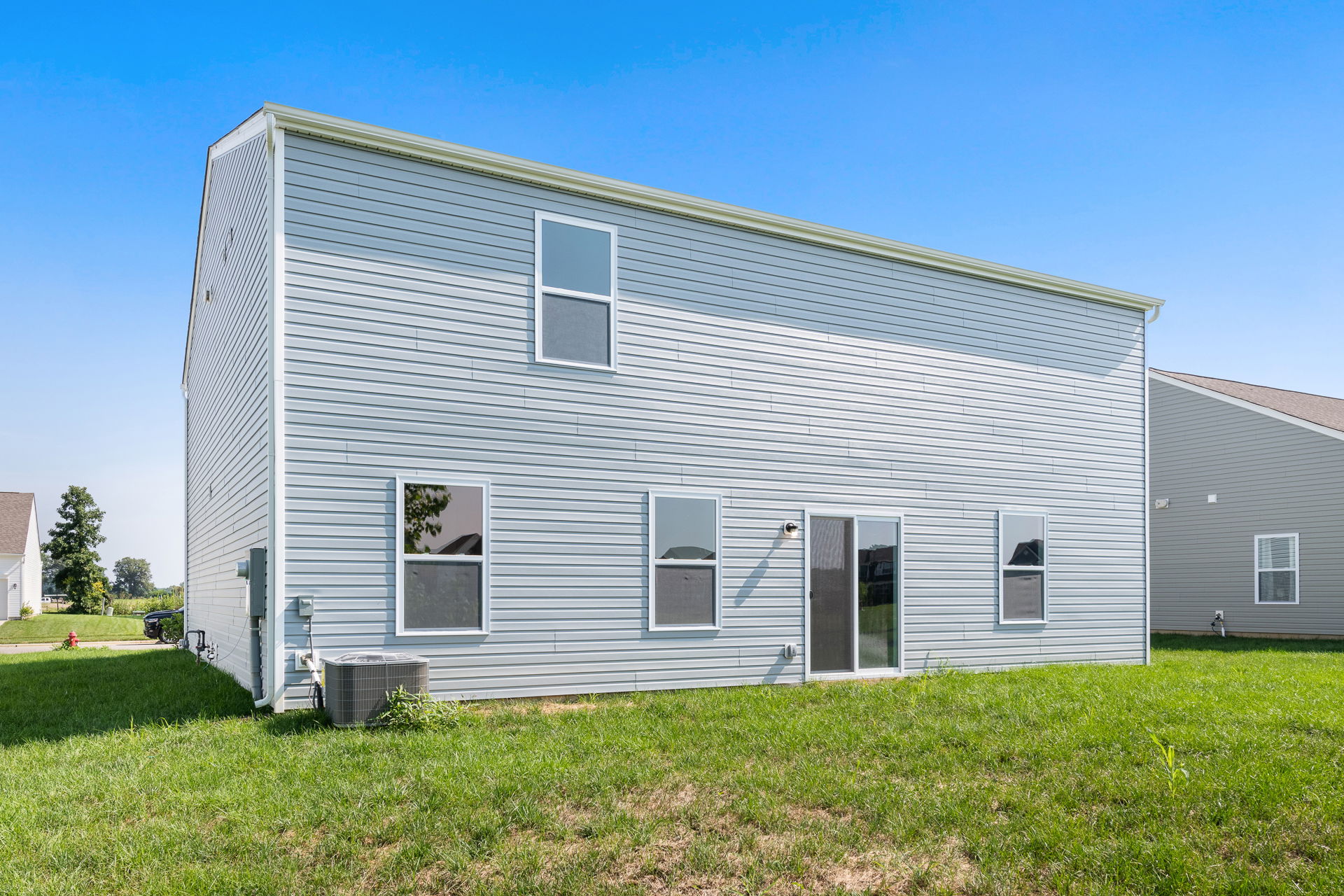 Modern two-story house exterior with gray siding and large windows on a sunny day.