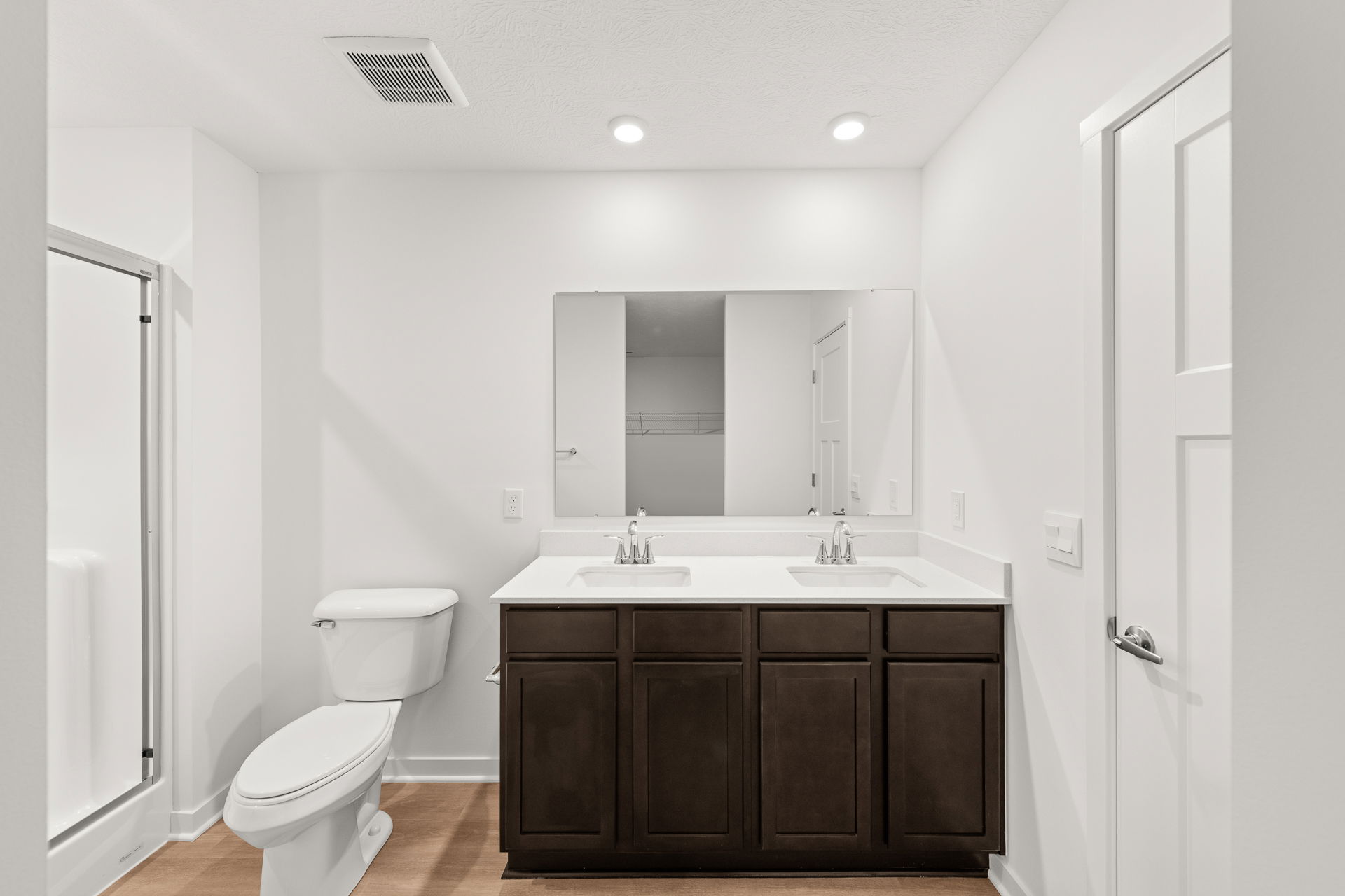 Modern bathroom featuring a dual sink vanity, white fixtures, and natural wood flooring.