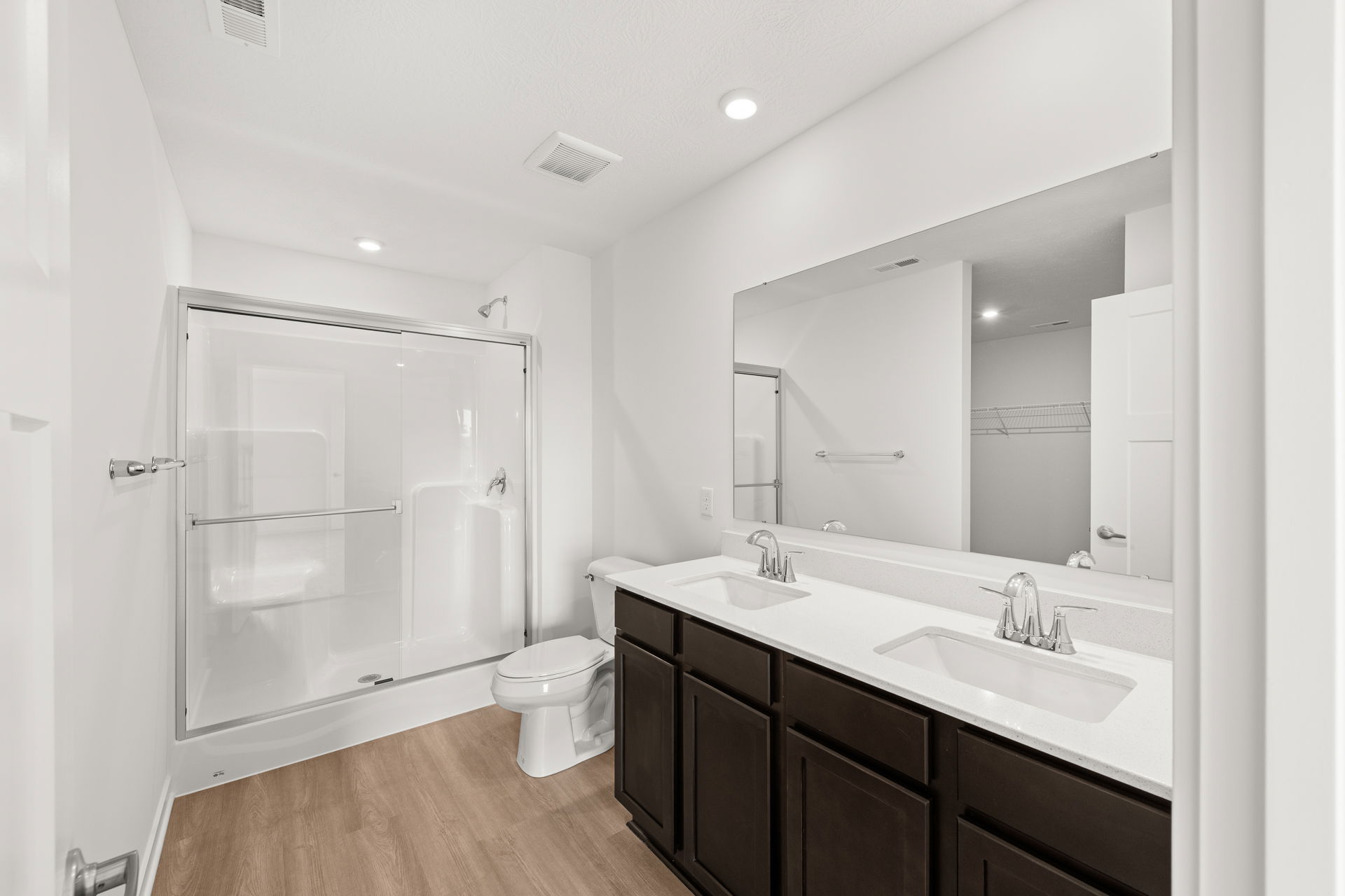 Modern bathroom featuring a glass shower, double vanity with quartz countertops, and wood-like flooring, ideal for contemporary home design.