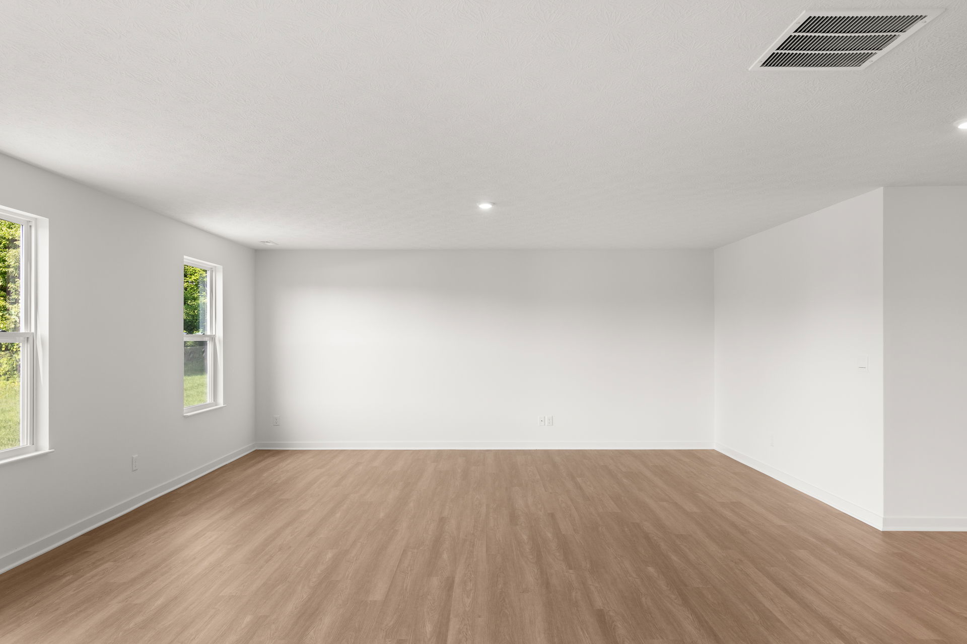 Spacious and bright empty living room with white walls and wood laminate flooring.