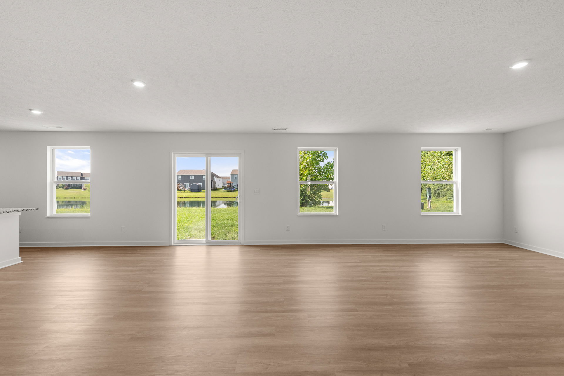 Spacious modern living room with large windows and sliding glass doors overlooking a tranquil backyard and pond.
