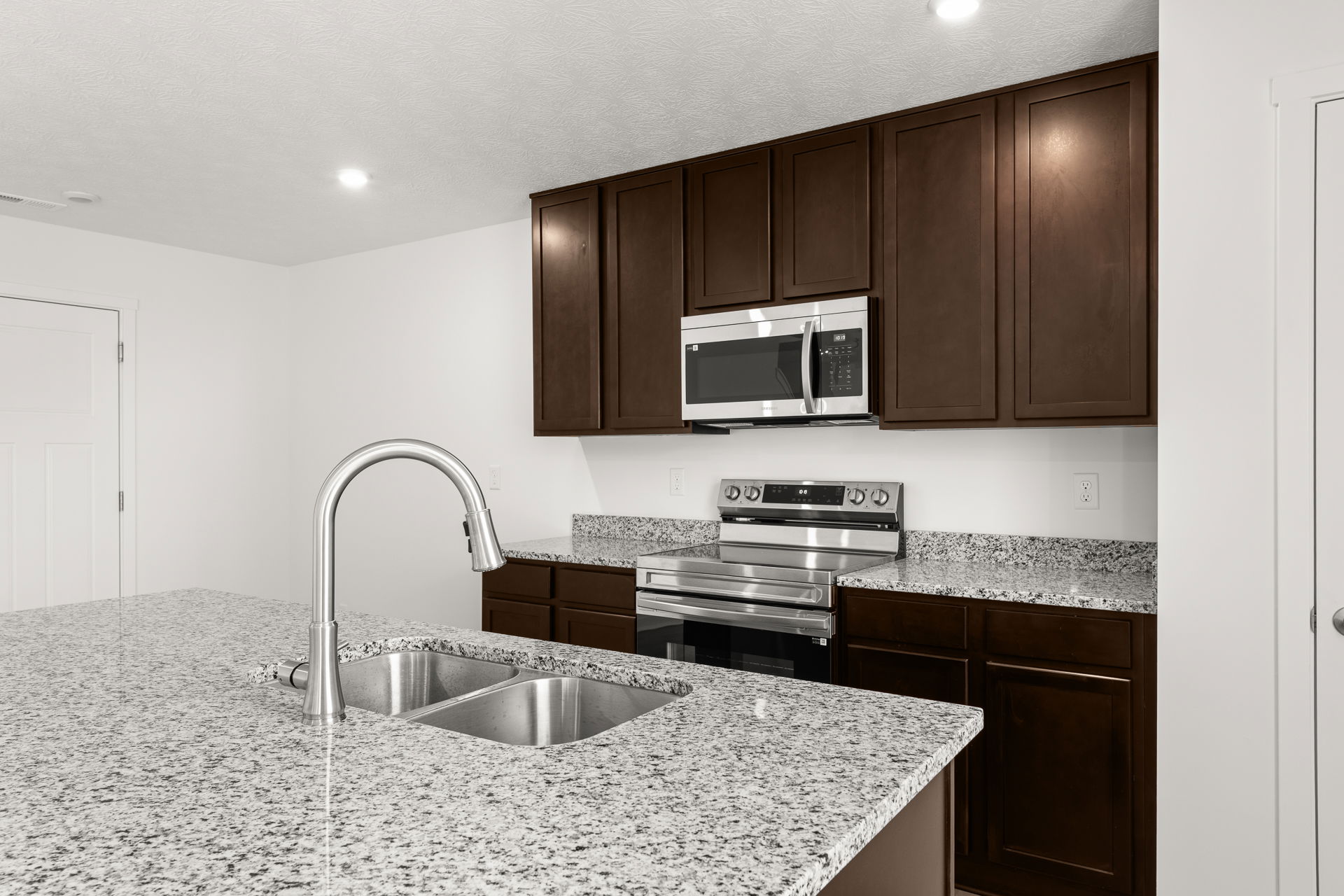Modern kitchen with dark wood cabinets, stainless steel appliances, and a granite countertop featuring a double sink.