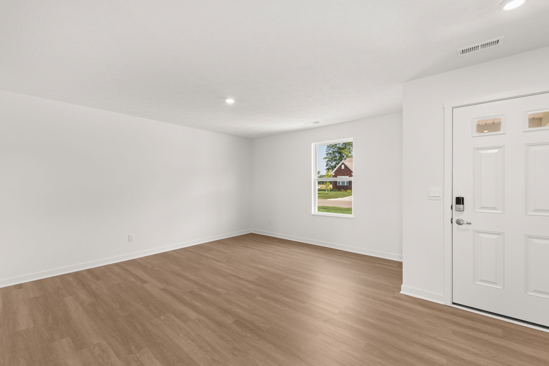 Bright and spacious living room with light-colored walls, modern wood flooring, and a large window offering outdoor views.