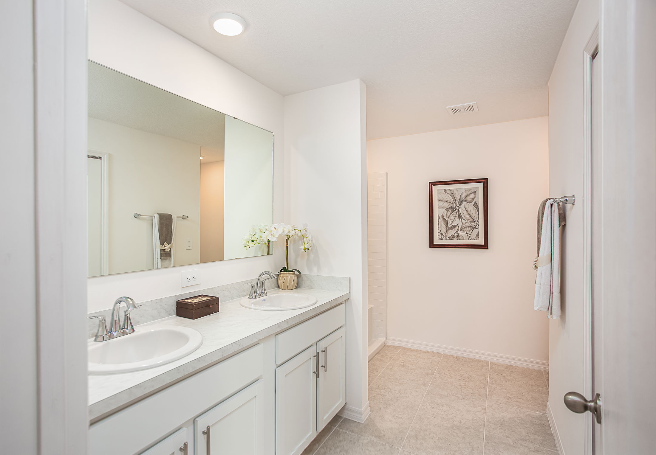 Modern bathroom with dual sinks, large mirror, and minimalist decor featuring white cabinets and tiled floors.